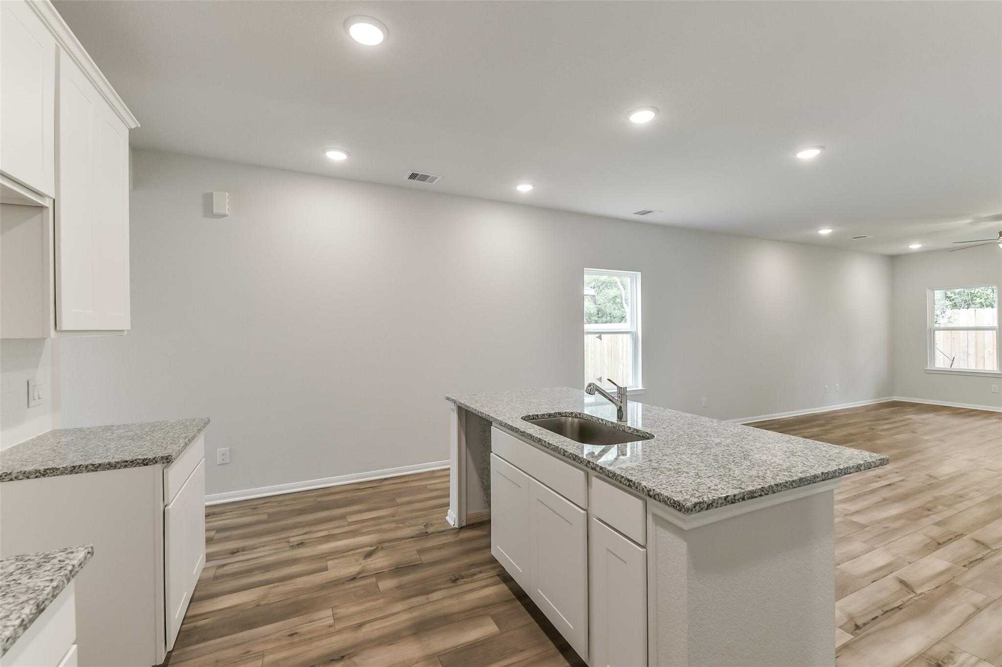 Modern kitchen featuring white cabinets, granite countertops, island sink, and hardwood floors in Davidson Homes The Sabine F, Conroe, Texas