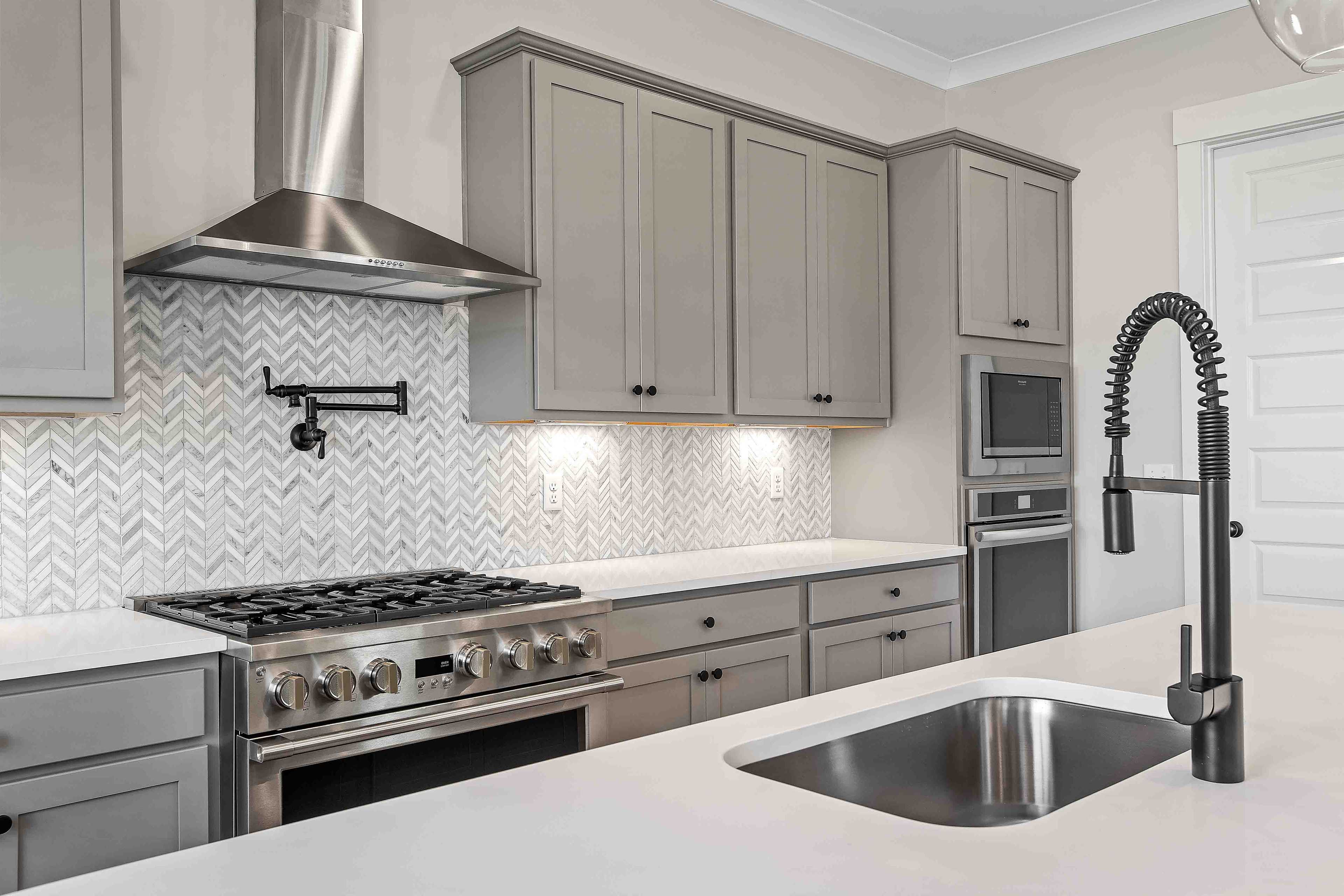 Modern kitchen in Shelton Square Murfreesboro TN featuring gray shaker cabinets, herringbone marble backsplash, and stainless steel appliances by Davidson Homes