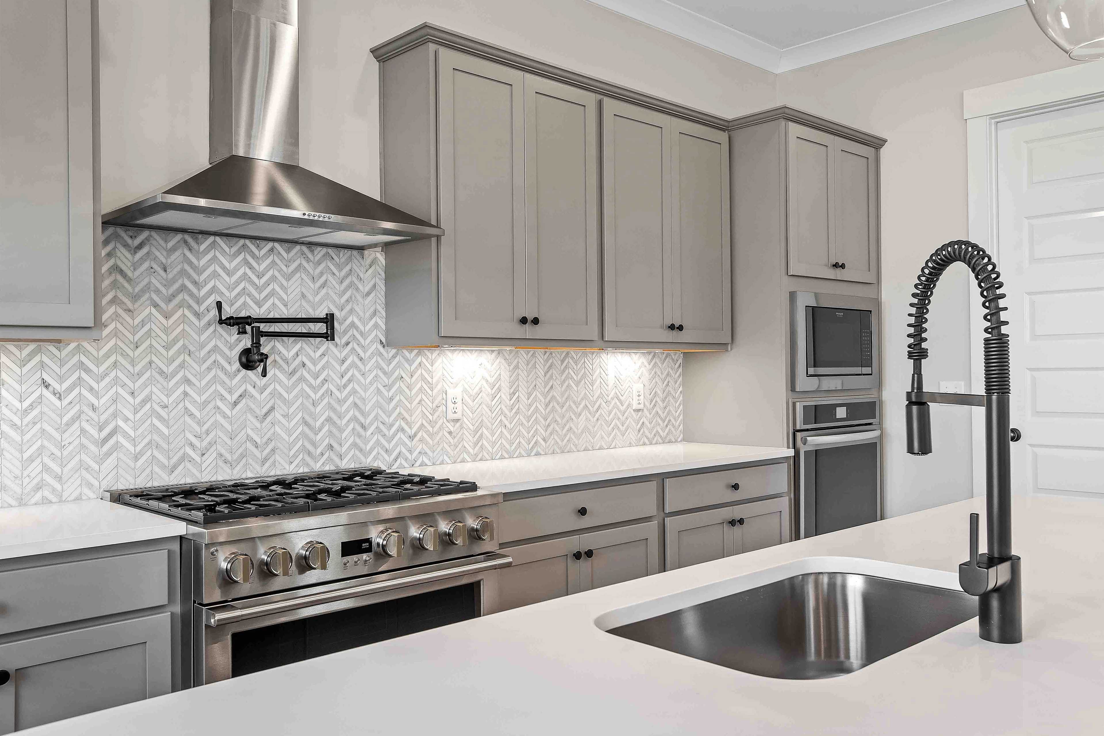 Modern kitchen in Shelton Square Murfreesboro TN featuring gray shaker cabinets, herringbone marble backsplash, and stainless steel appliances by Davidson Homes