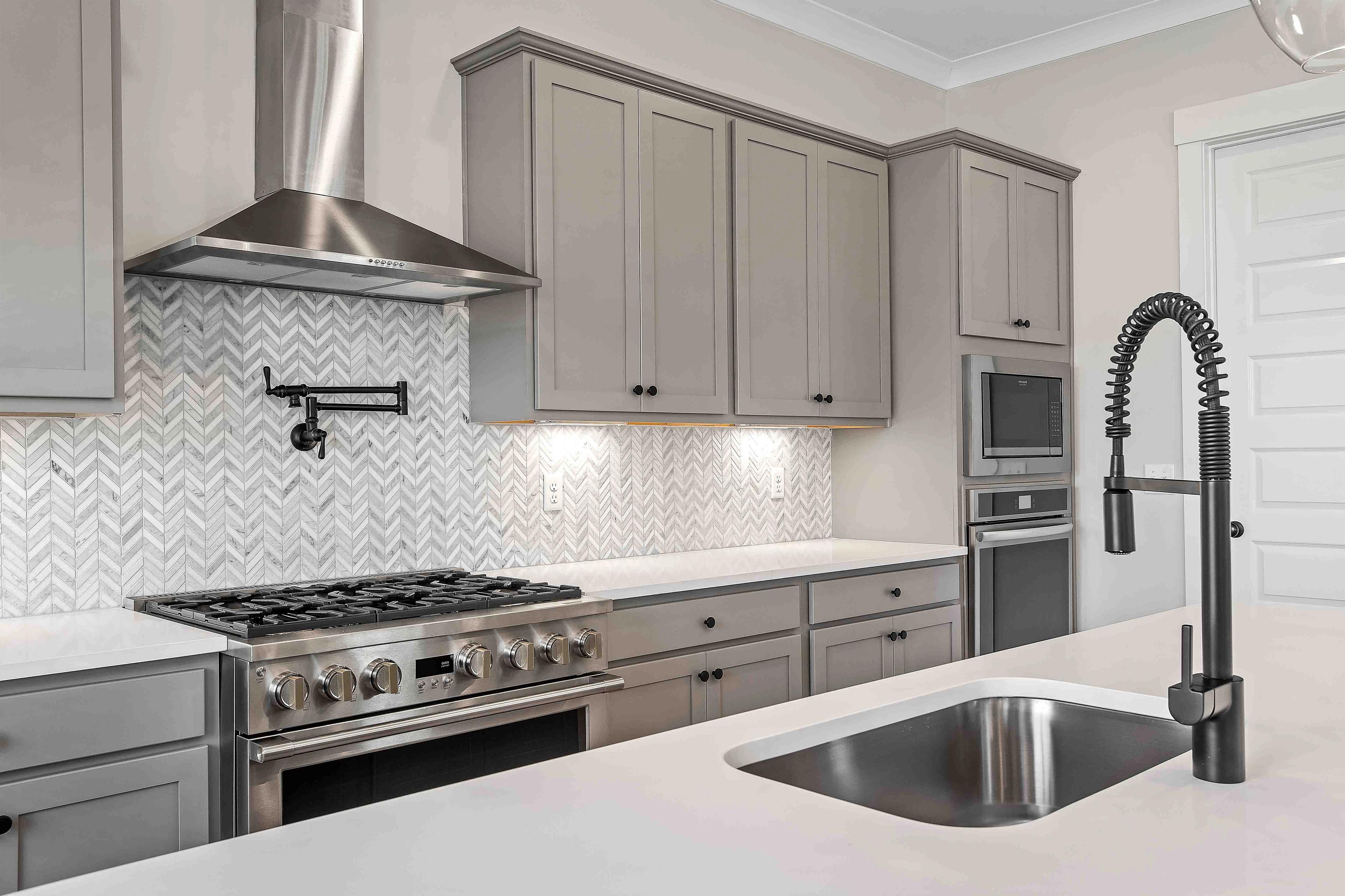 Modern kitchen in Shelton Square Murfreesboro TN featuring gray shaker cabinets, herringbone marble backsplash, and stainless steel appliances by Davidson Homes