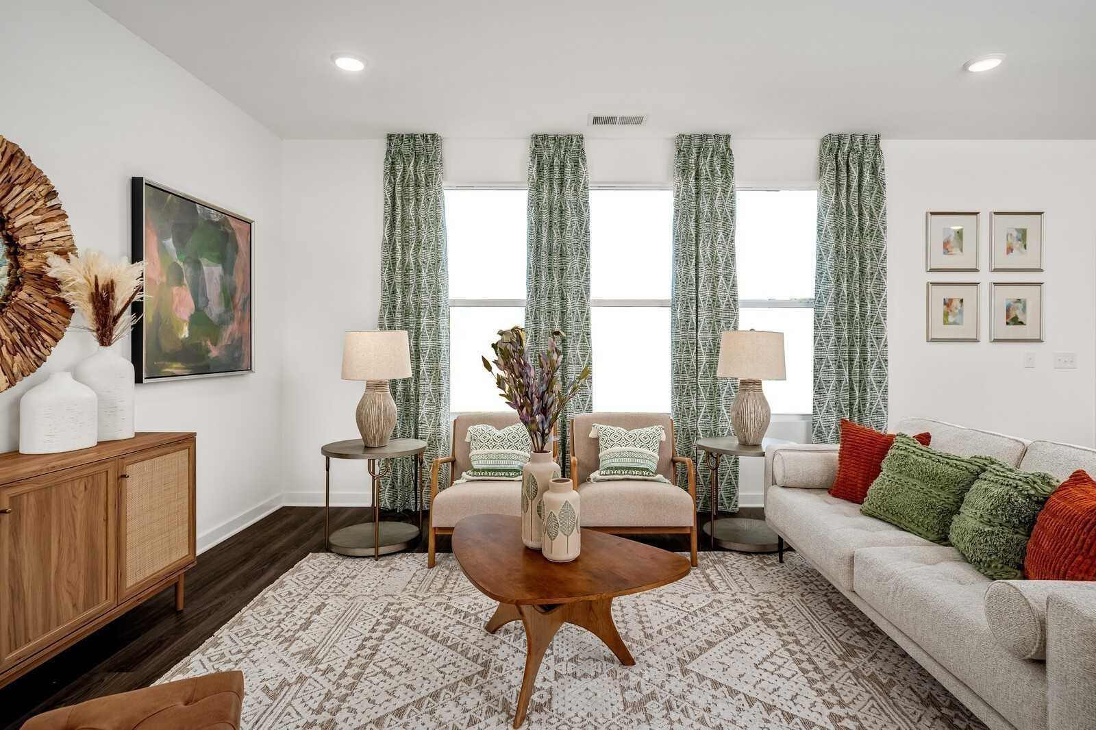 Cozy living room with beige sofa, green pillows, wooden coffee table, and large curtained windows in Davidson Homes The Gordon B, White House, TN