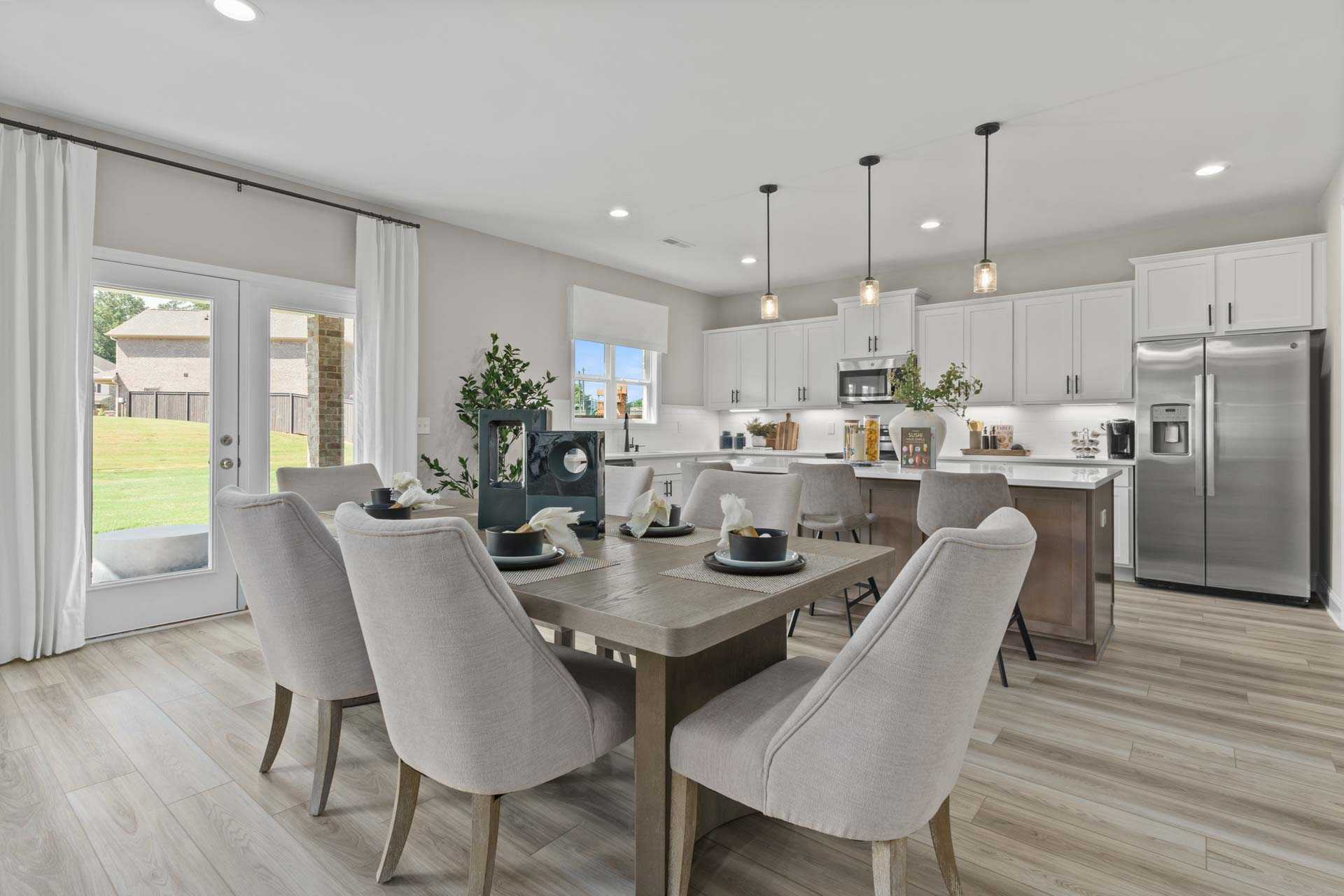 Spacious open-concept kitchen and dining area at Creek Grove in New Market Alabama with white cabinets hardwood floors and French doors