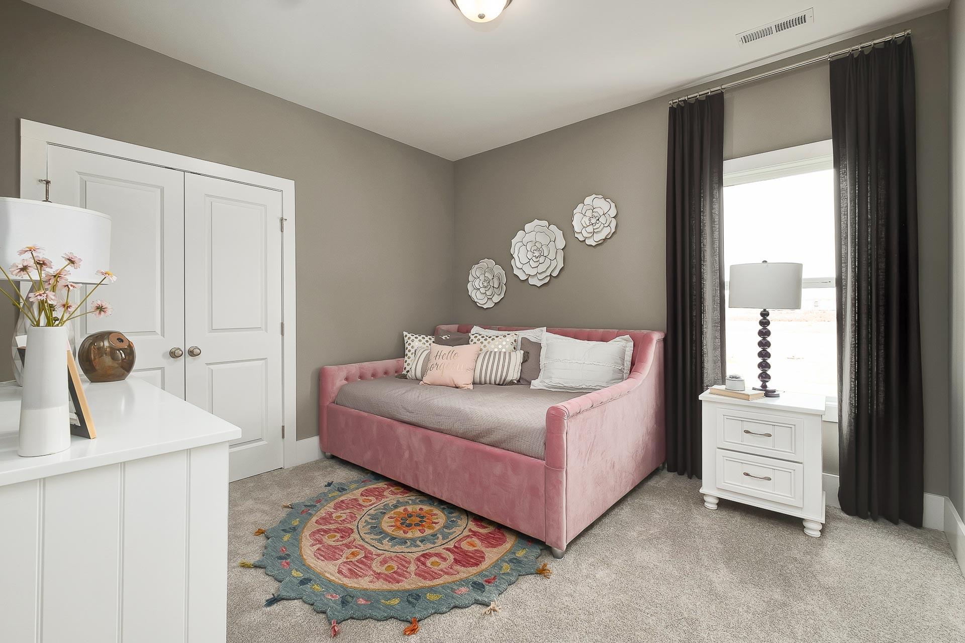 Cozy secondary bedroom in The Everett with pink velvet daybed, white dresser, floral decor and gray walls