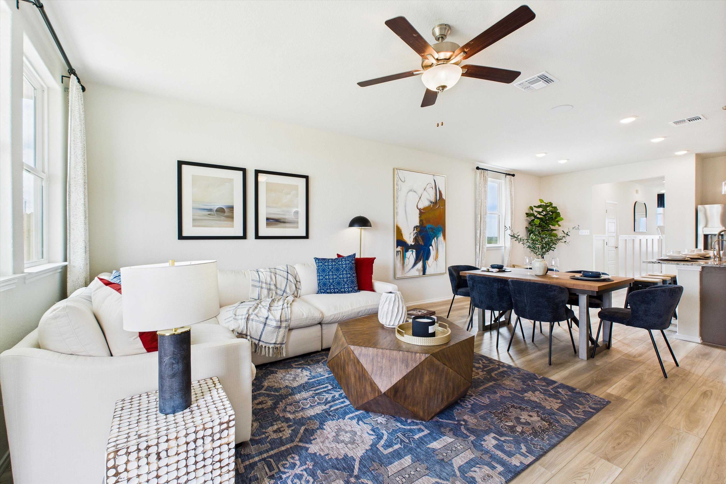 Open-concept living and dining area in Agave San Antonio TX home by Davidson Homes featuring white sectional sofa, blue rug, and hardwood floors