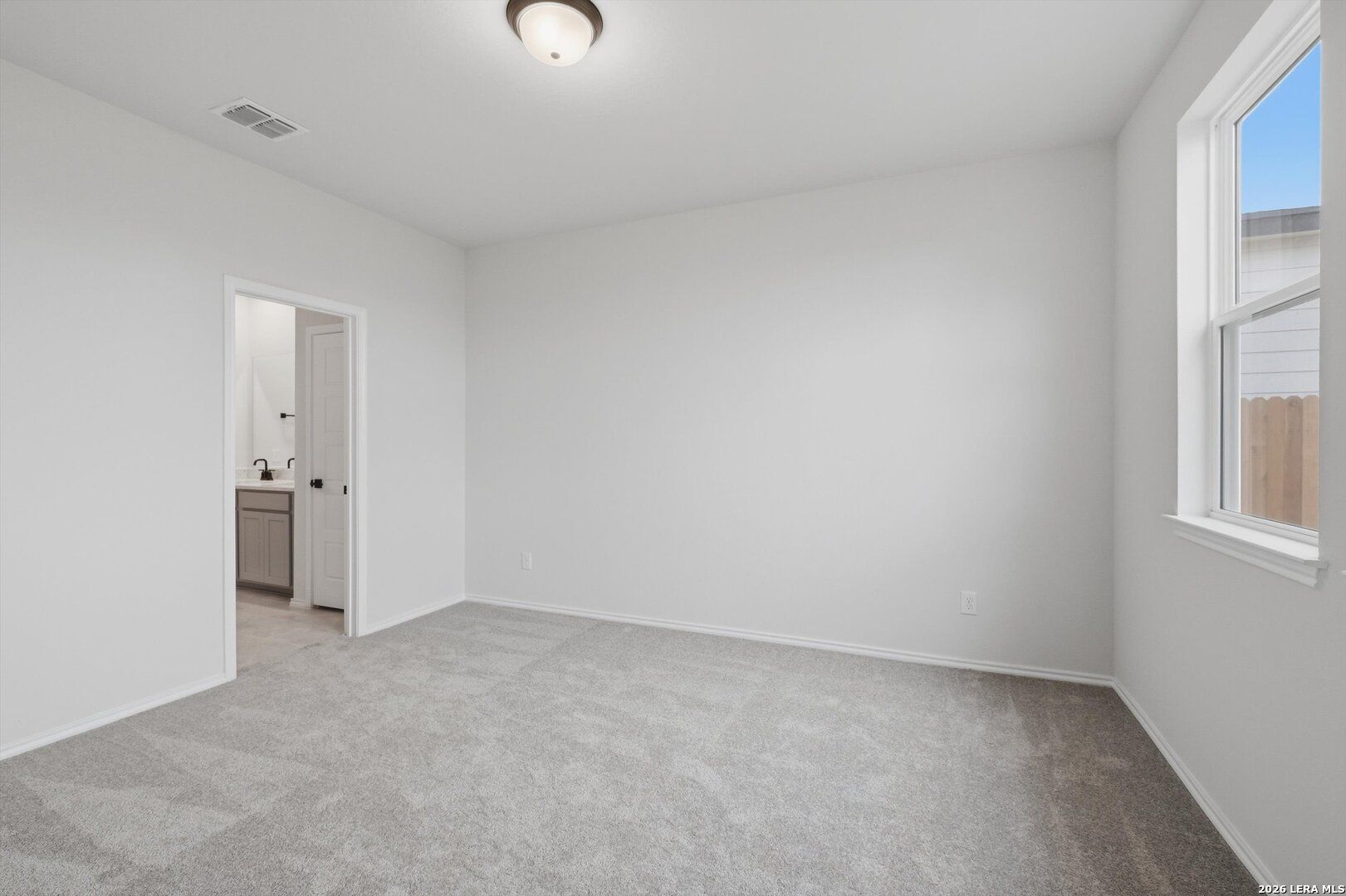 Bright bedroom with white walls, gray carpet, large window, and en-suite bathroom in Davidson Homes The Blanco C, San Antonio, Texas