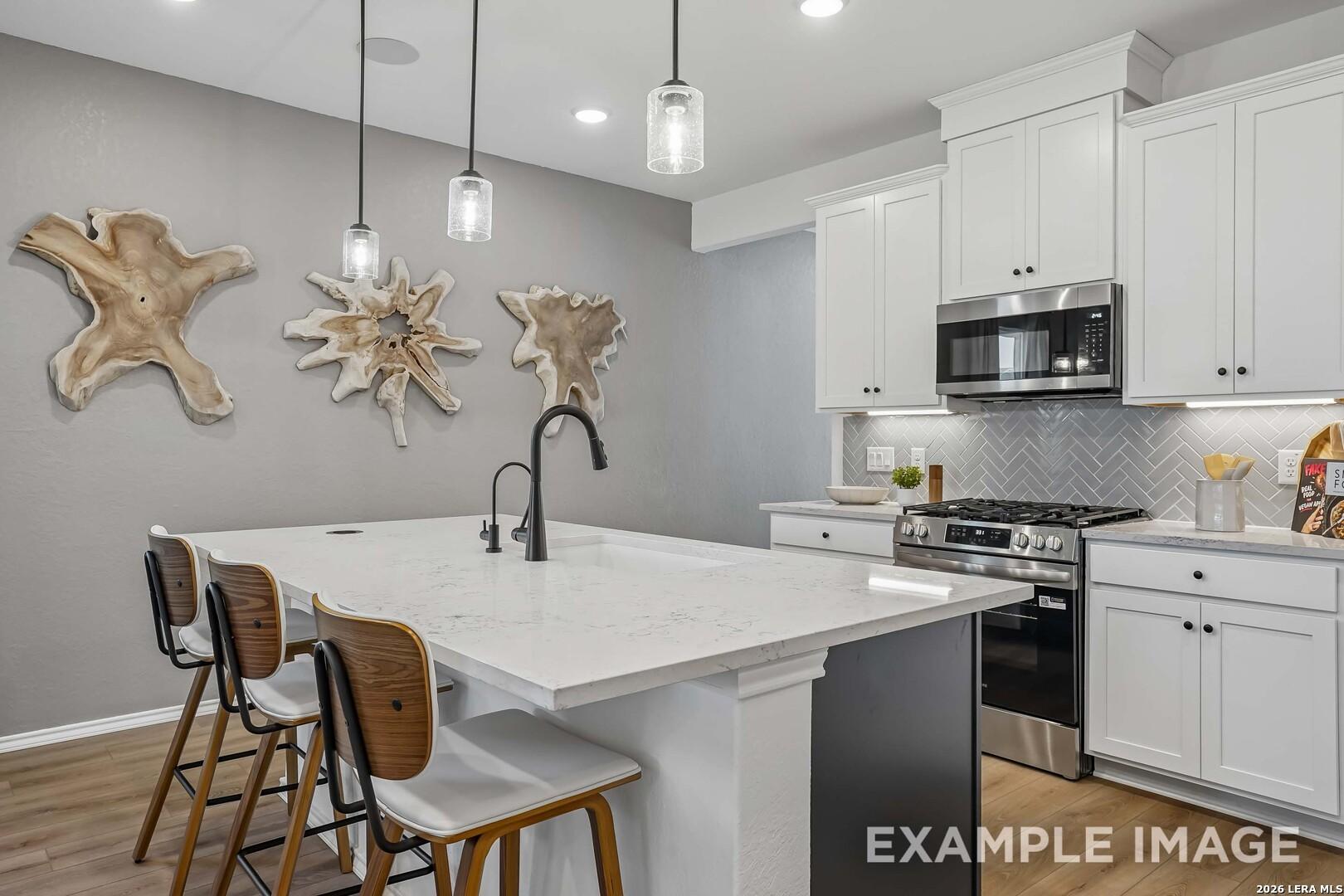 Modern kitchen with white quartz island, black pendant lights, and stainless appliances in Davidson Homes' Pinecrest F, San Antonio