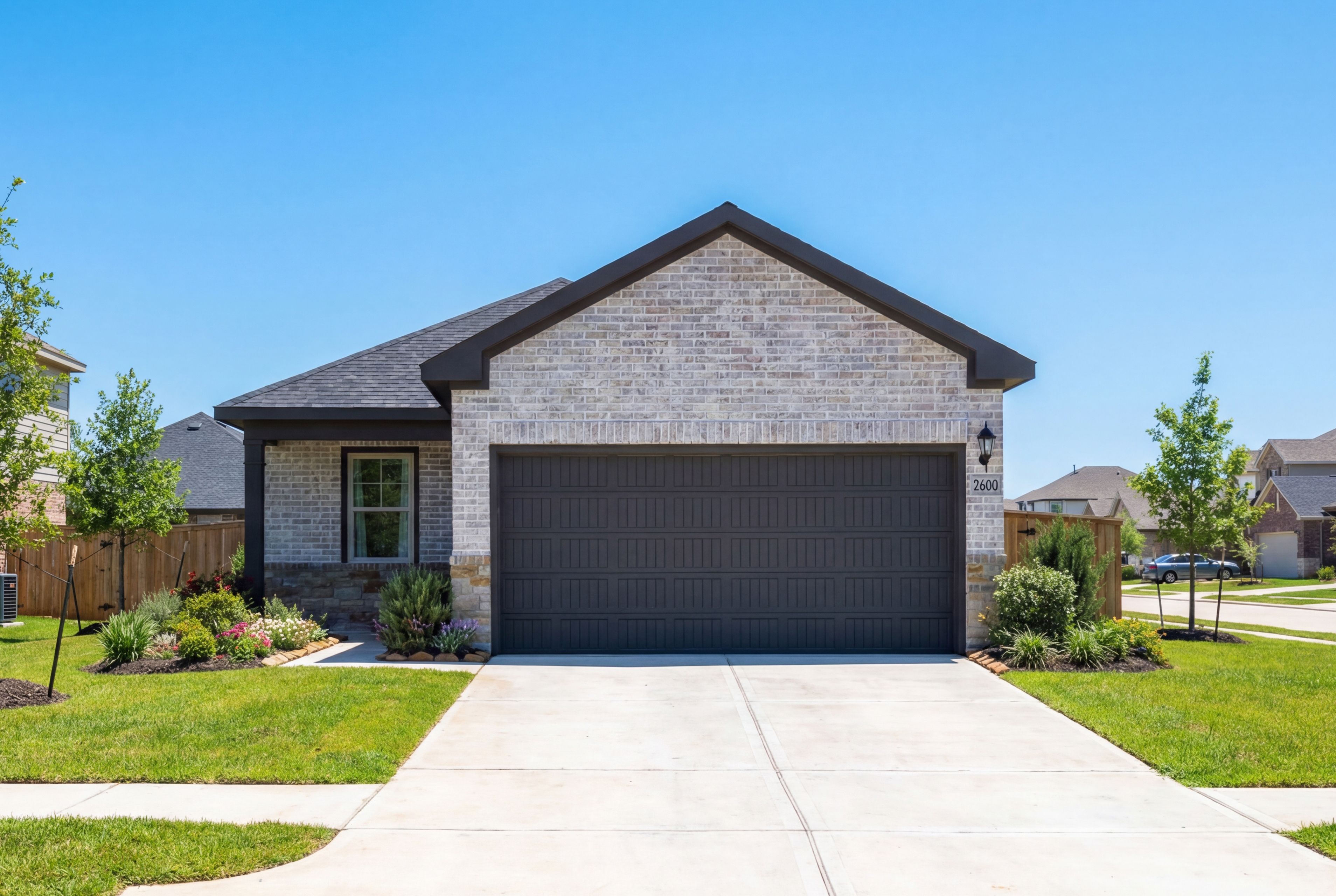 The Comal G single-story home front elevation with white brick exterior, dark 2-car garage, and landscaped yard in Magnolia Texas