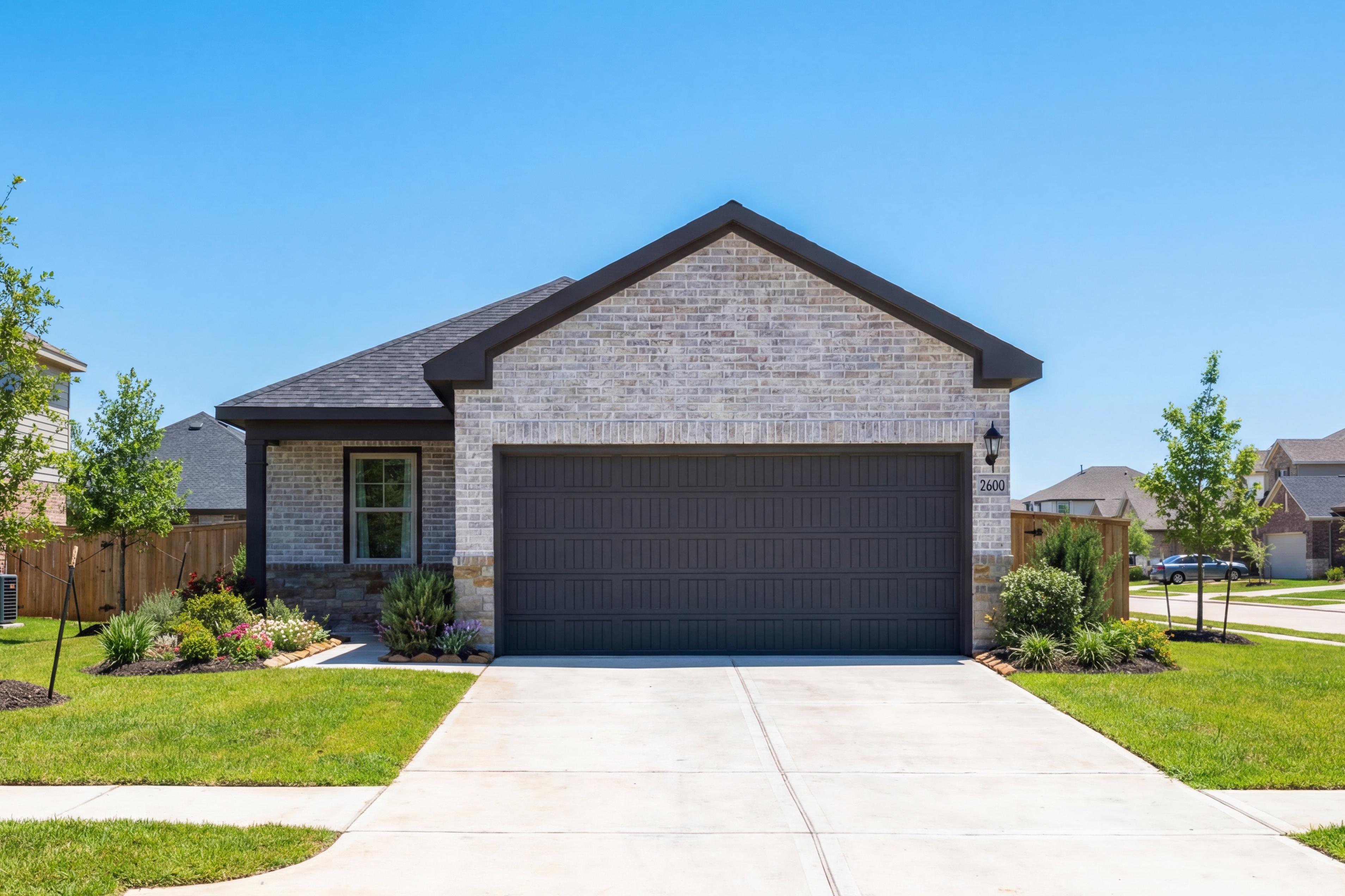 The Comal G single-story home front elevation with white brick exterior, dark 2-car garage, and landscaped yard in Magnolia Texas