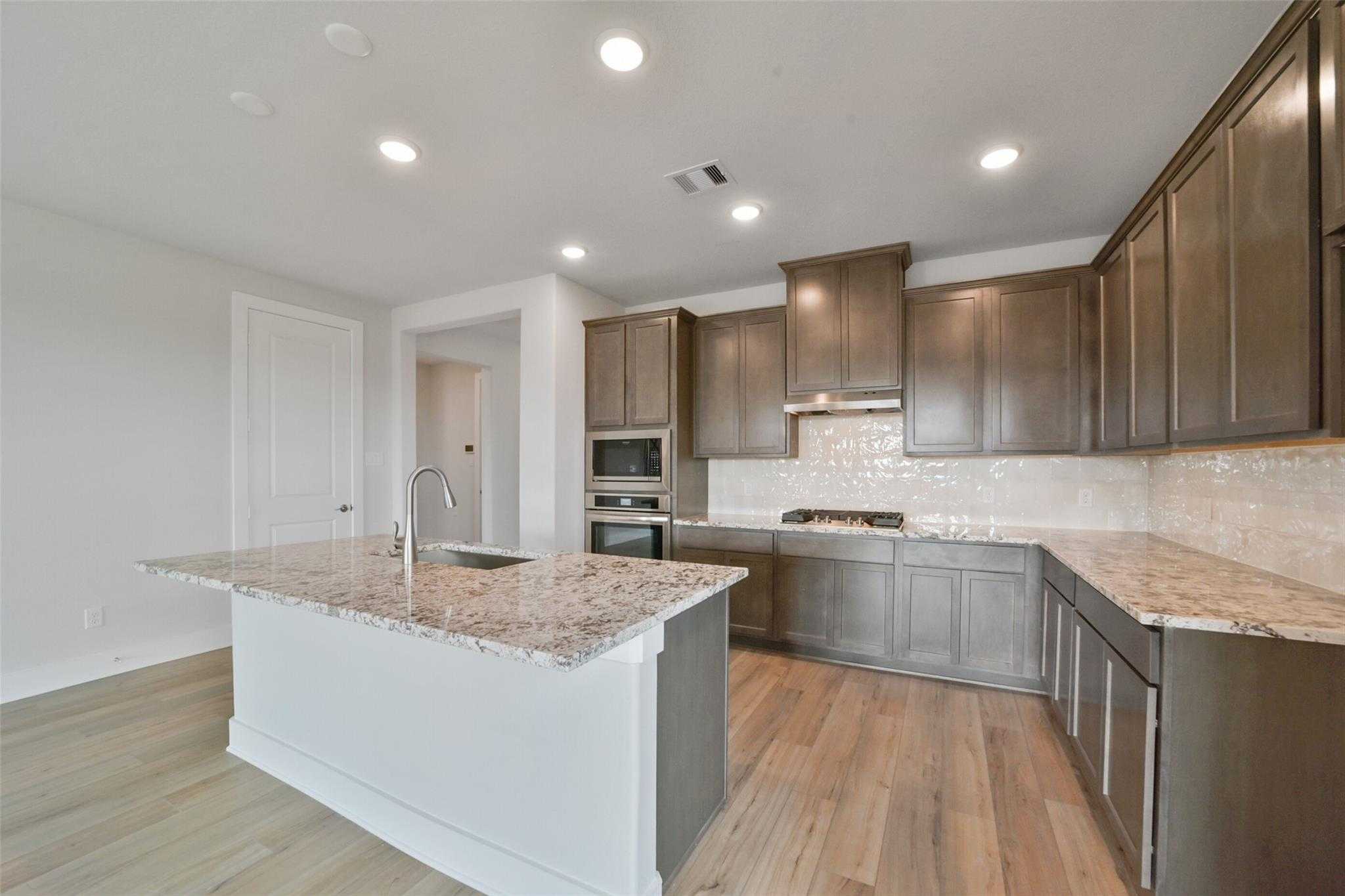 Modern open-concept kitchen with granite island, stainless appliances, and shaker cabinets in Davidson Homes The Zion A, Lago Mar