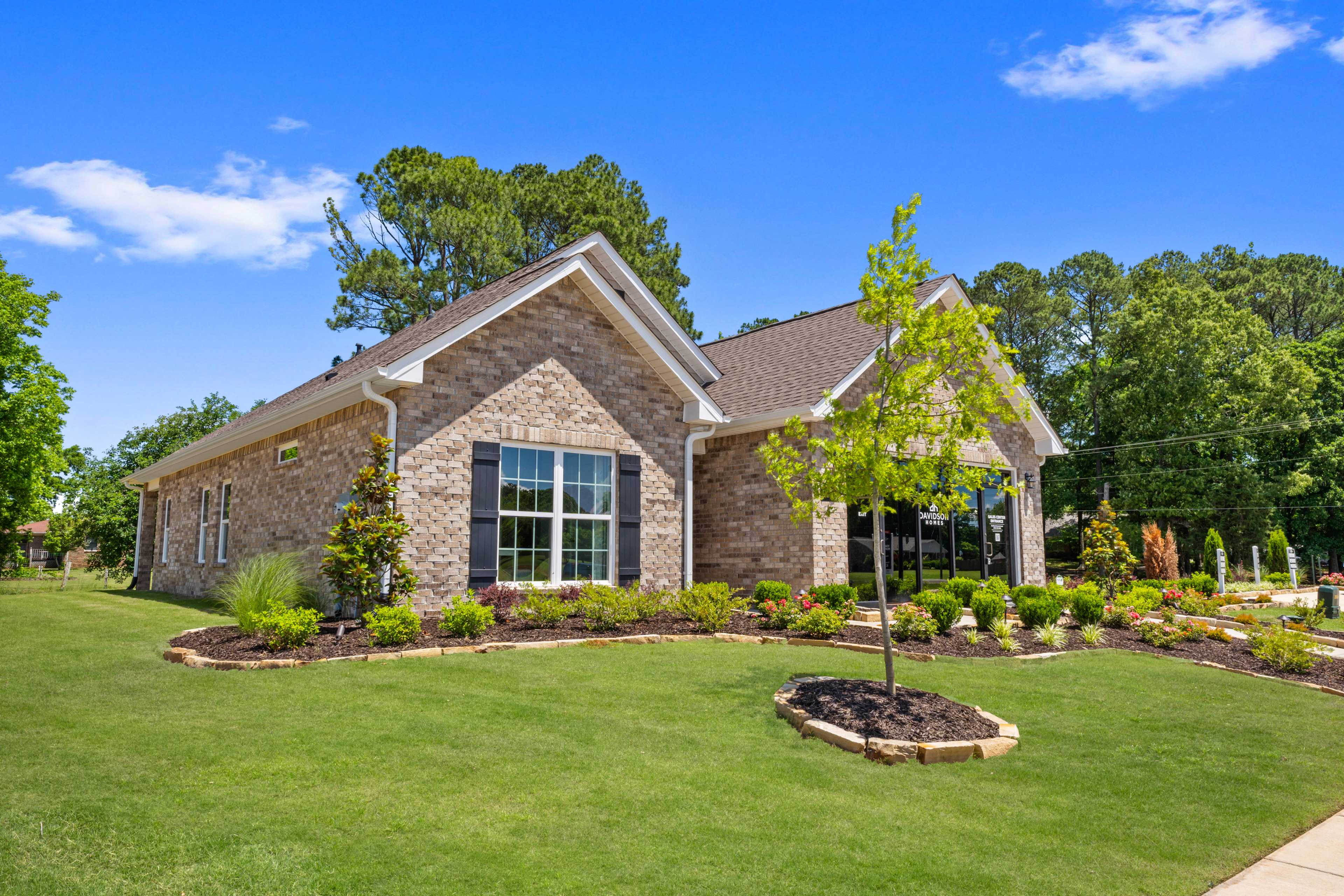 Single-story brick home exterior at Hollon Meadow in Decatur Alabama with shuttered windows, lush landscaping, and green lawn