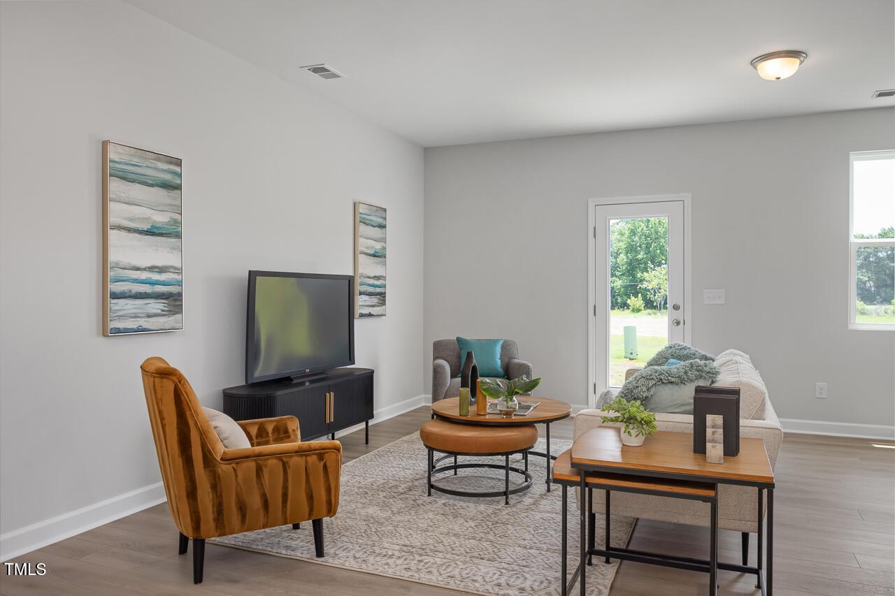 Cozy living room with gray walls, mounted TV, orange armchair, beige sofa, and French doors to backyard in Davidson Homes The Warren, Fuquay-Varina, NC