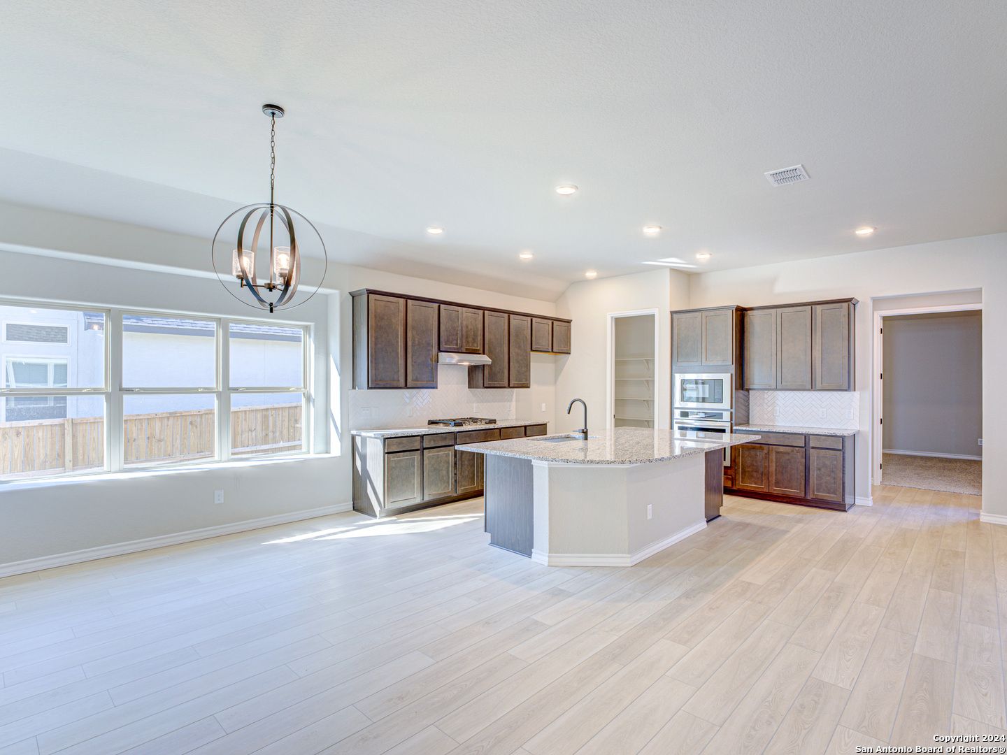 Spacious open kitchen with quartz island, shaker cabinets, stainless appliances, and large windows in Davidson Homes Summerlin A, Castroville, Texas