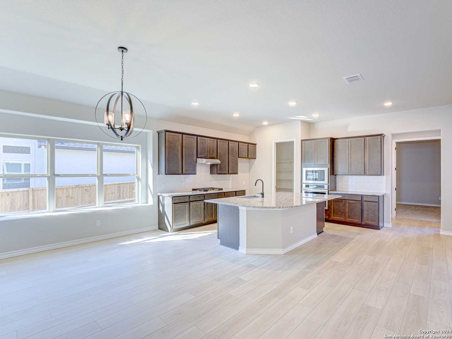 Spacious open kitchen with quartz island, shaker cabinets, stainless appliances, and large windows in Davidson Homes Summerlin A, Castroville, Texas