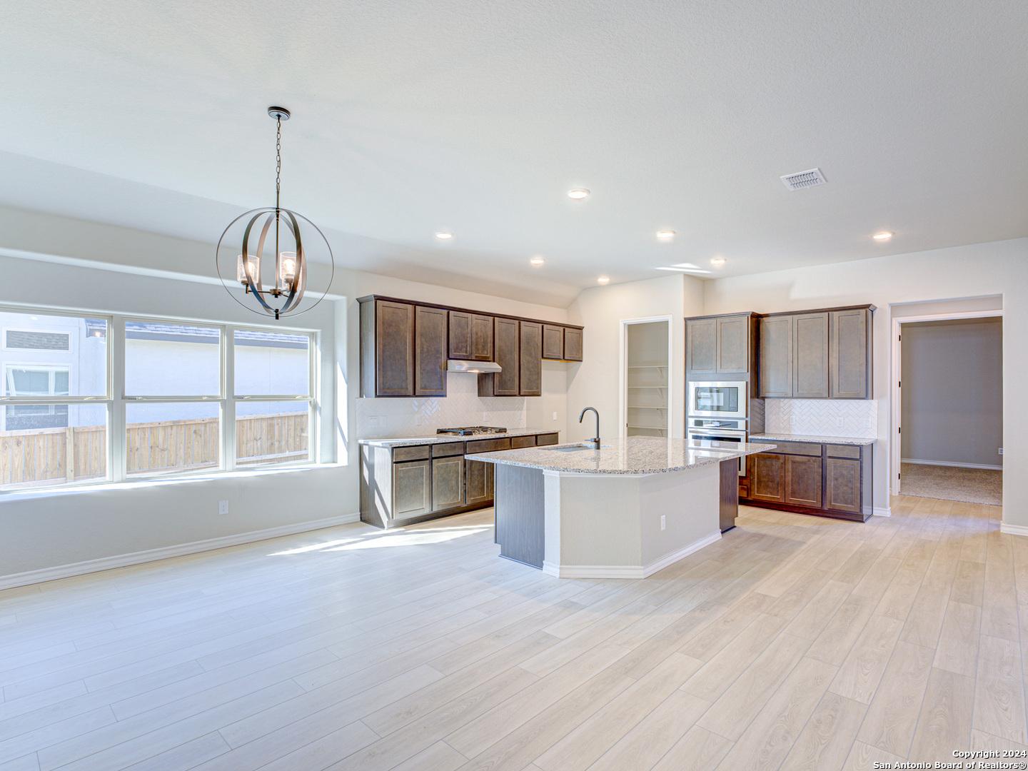 Spacious open kitchen with quartz island, shaker cabinets, stainless appliances, and large windows in Davidson Homes Summerlin A, Castroville, Texas