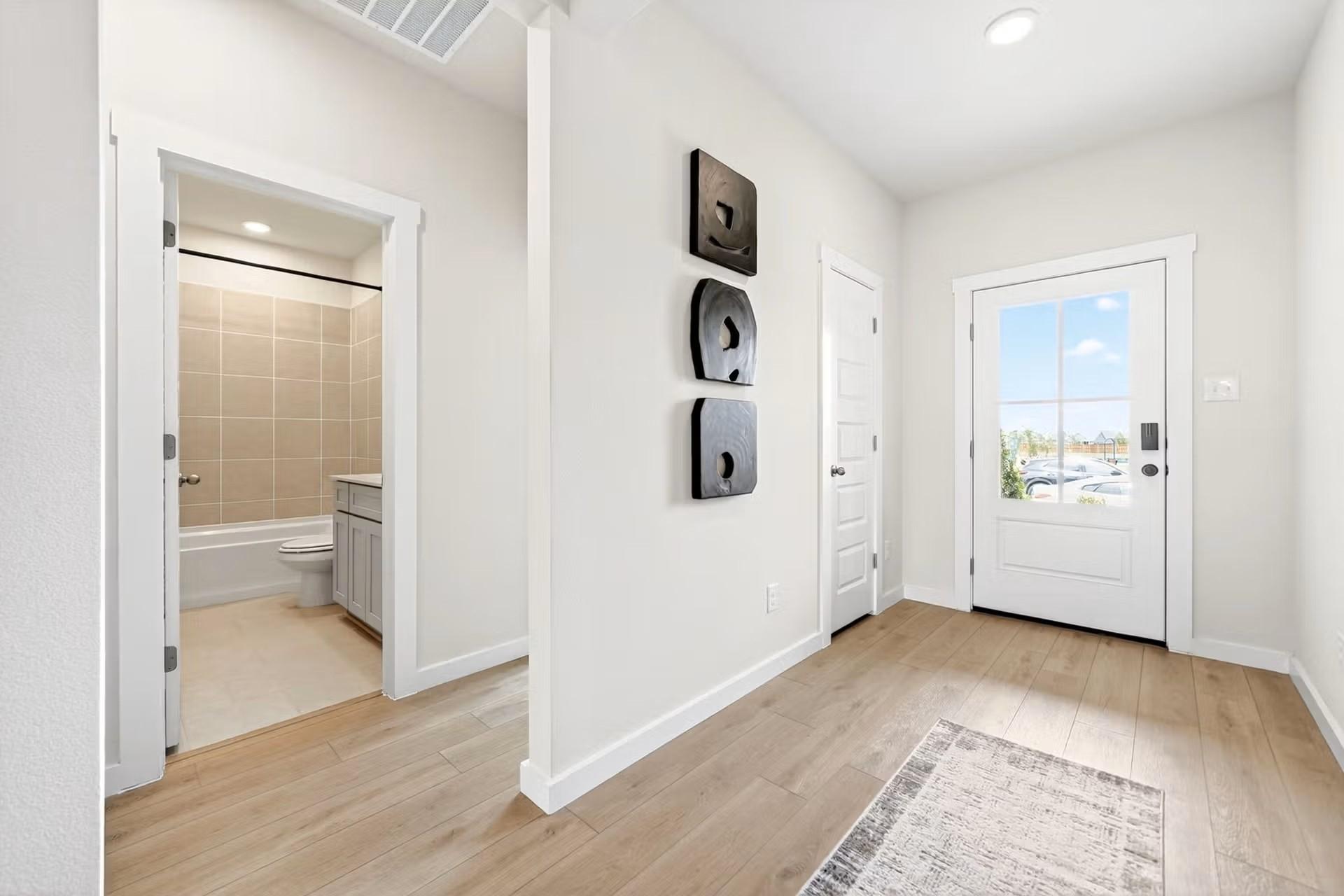 Bright entryway with wood-look flooring leading to a full bathroom in The Laurel I floor plan by Davidson Homes in Heartland.