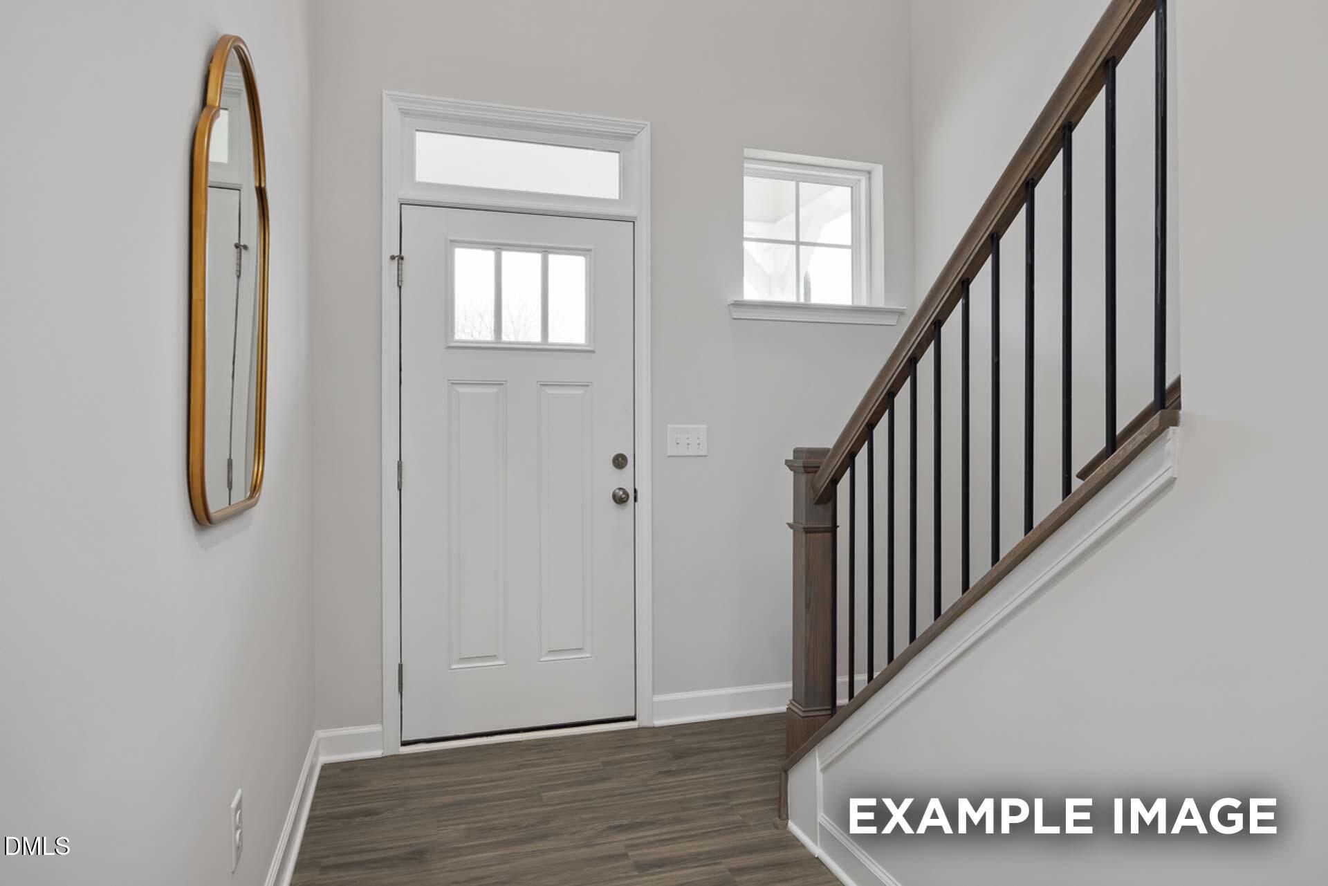 Welcoming entry foyer with white paneled door, arched gold mirror, and wooden staircase in Davidson Homes The Gavin C, Lillington, NC