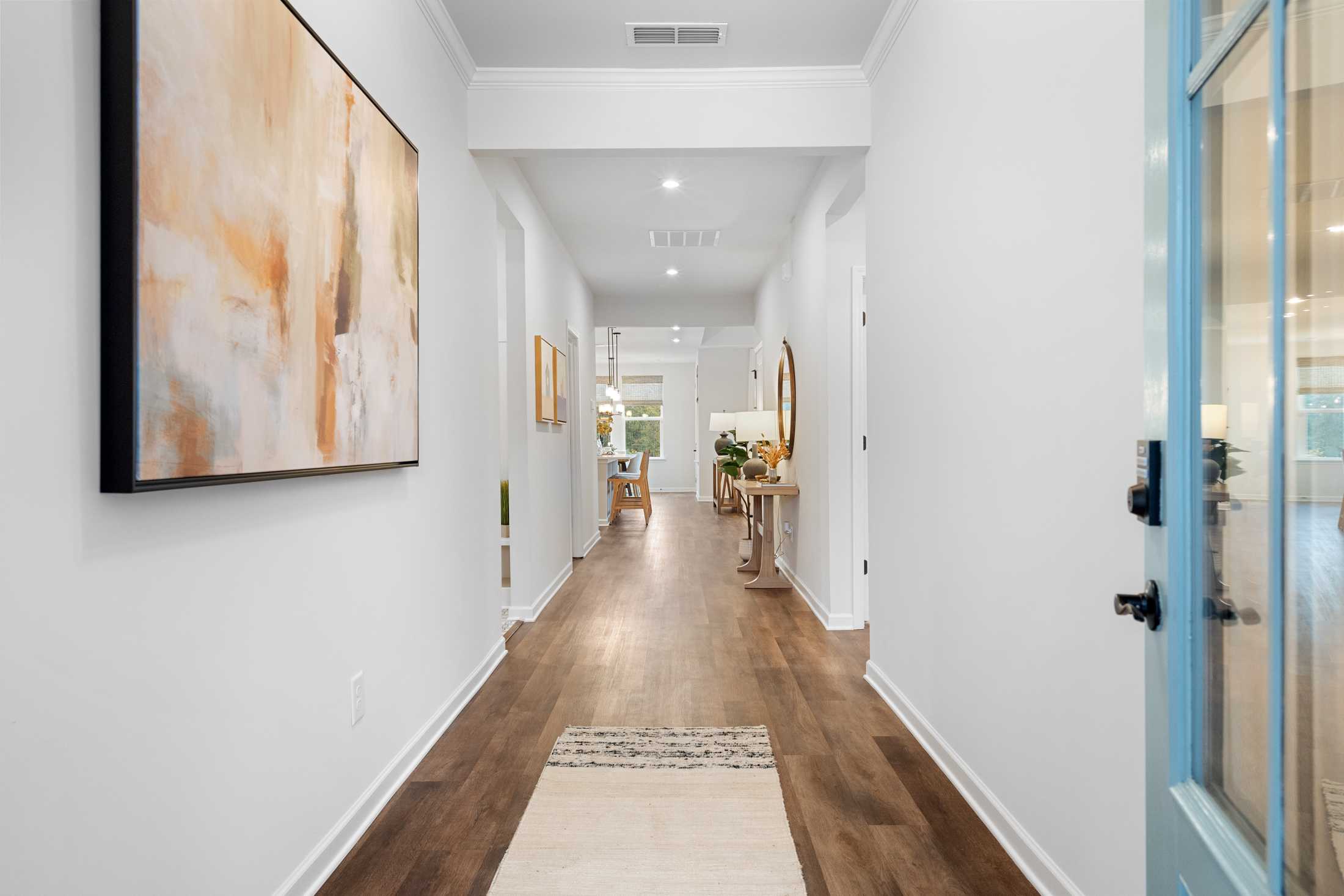 Spacious hallway in The Edison C home featuring hardwood floors, white walls, abstract artwork, and blue entry door