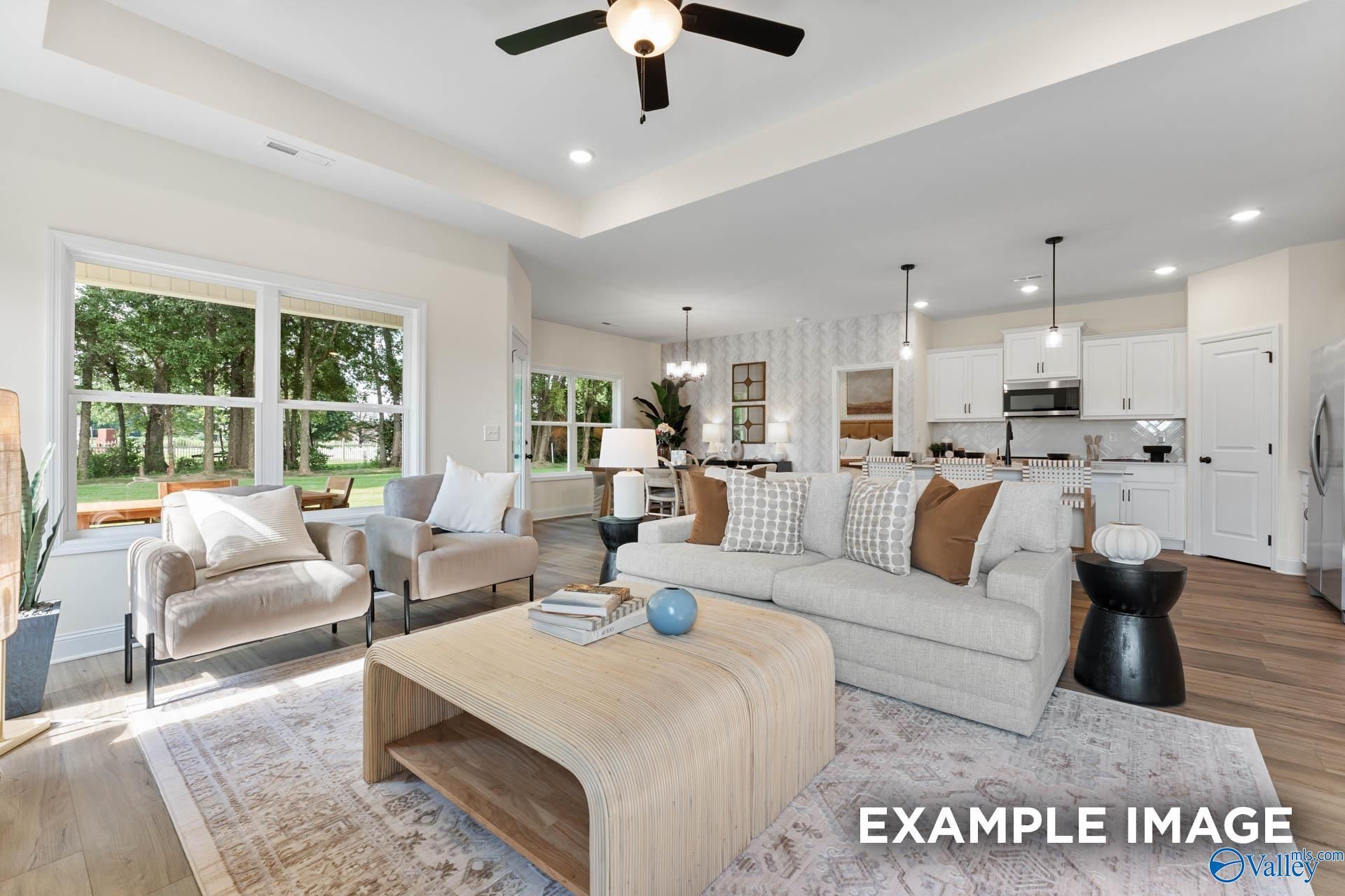 Cozy open living room with beige sofa, armchairs, coffee table, and adjacent white kitchen in Davidson Homes The Franklin, Huntsville AL