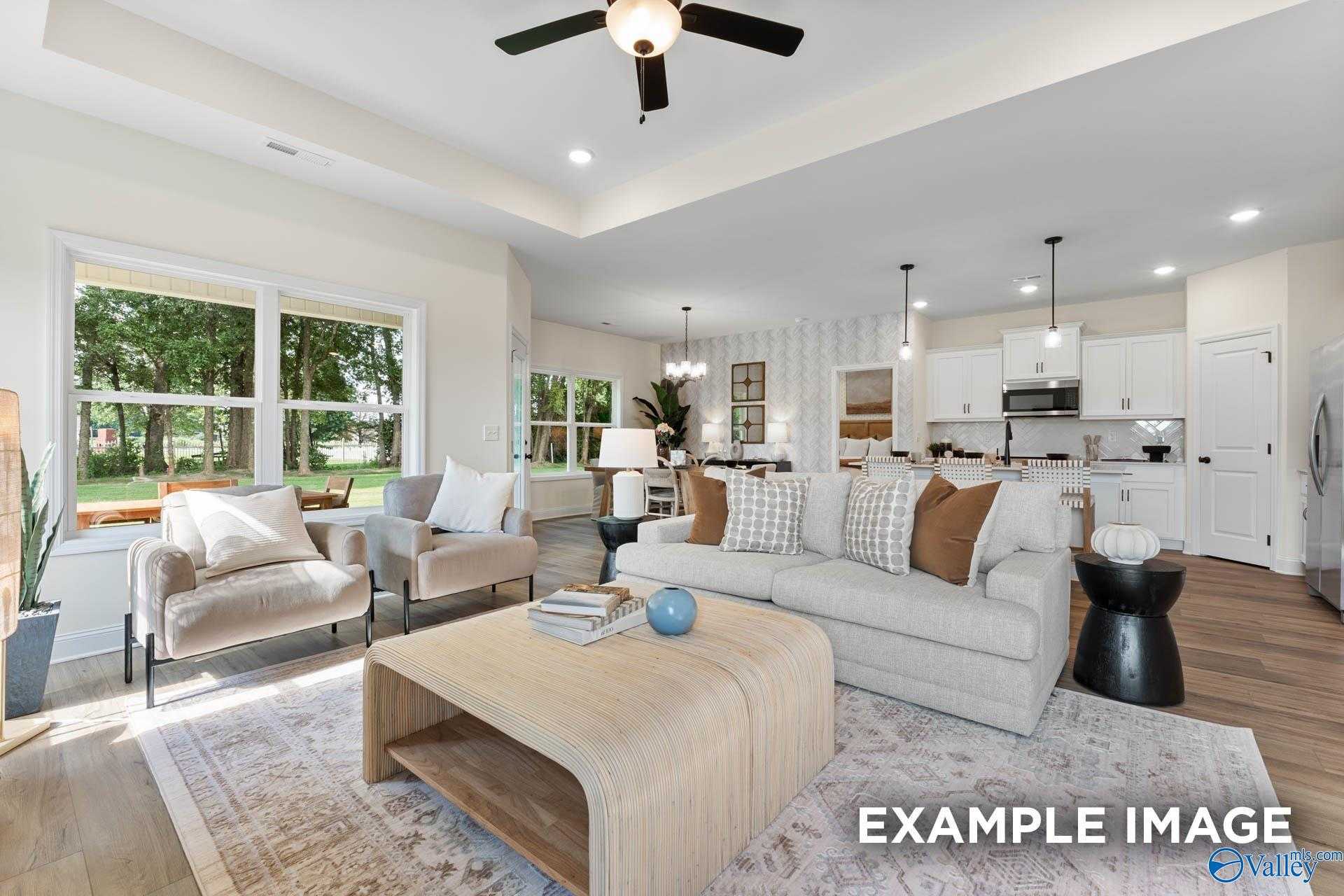 Open-concept living room with beige sofa, ceiling fan, large windows, and kitchen view in The Franklin 3-bedroom home, Huntsville, AL