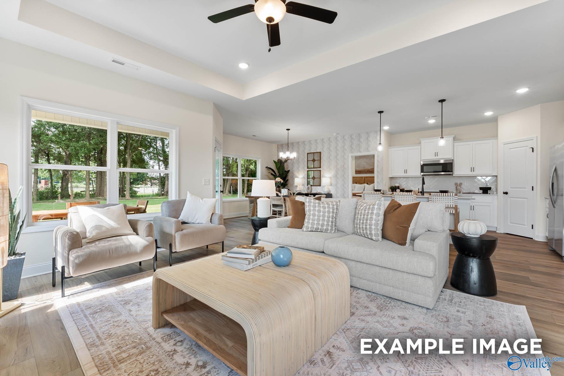 Cozy open living room with beige sofa, armchairs, coffee table, and adjacent white kitchen in Davidson Homes The Franklin, Huntsville AL
