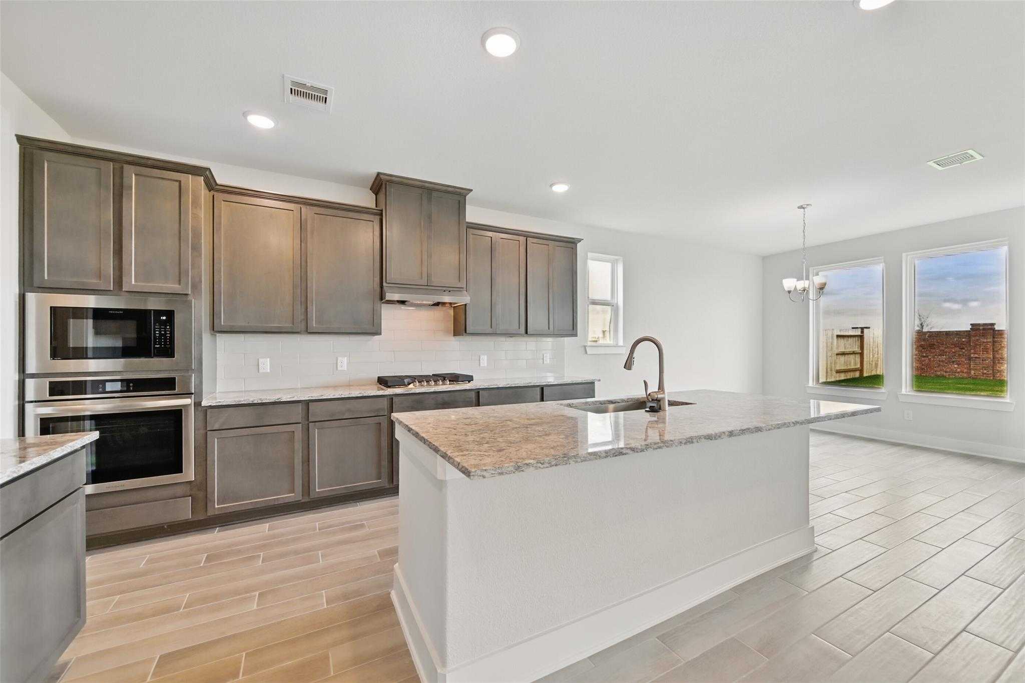 Modern kitchen featuring gray shaker cabinets, granite island, stainless double oven and gas range in Davidson Homes The Philip A, Lago Mar