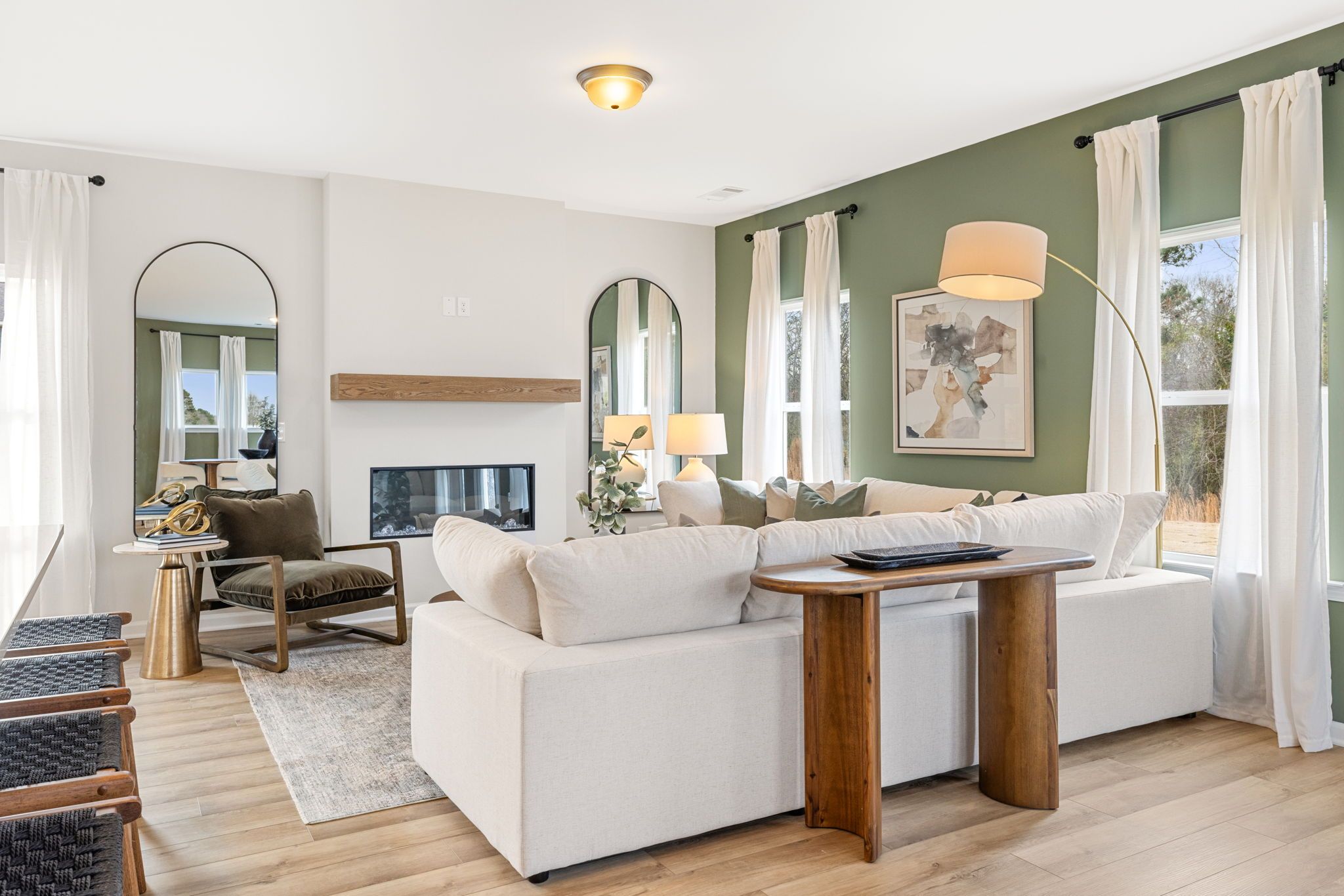 Cozy modern living room at Links Crossing in Auburn Alabama with white sectional sofa, wood coffee table, green accent wall, arched mirrors and fireplace