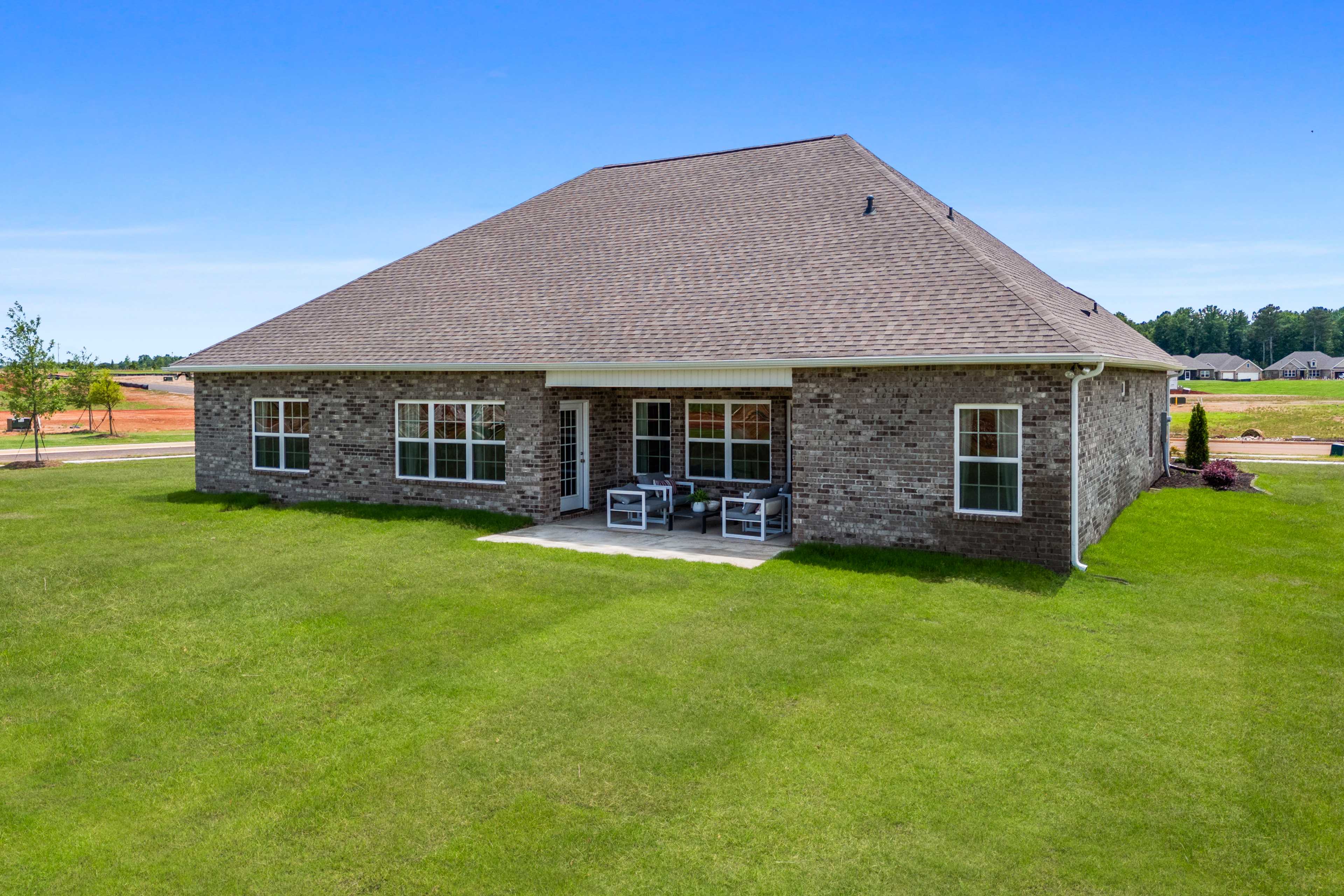Spacious brick home backyard at Creekside in Harvest Alabama with covered patio, seating and lush green lawn