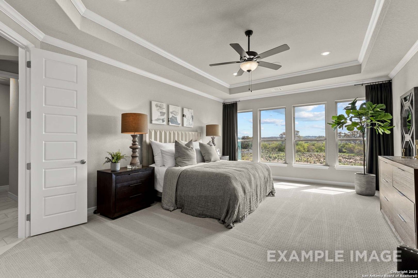 Elegant master bedroom with king bed, tray ceiling, ceiling fan, and large windows in Davidson Homes The Summerlin B, Castroville, Texas