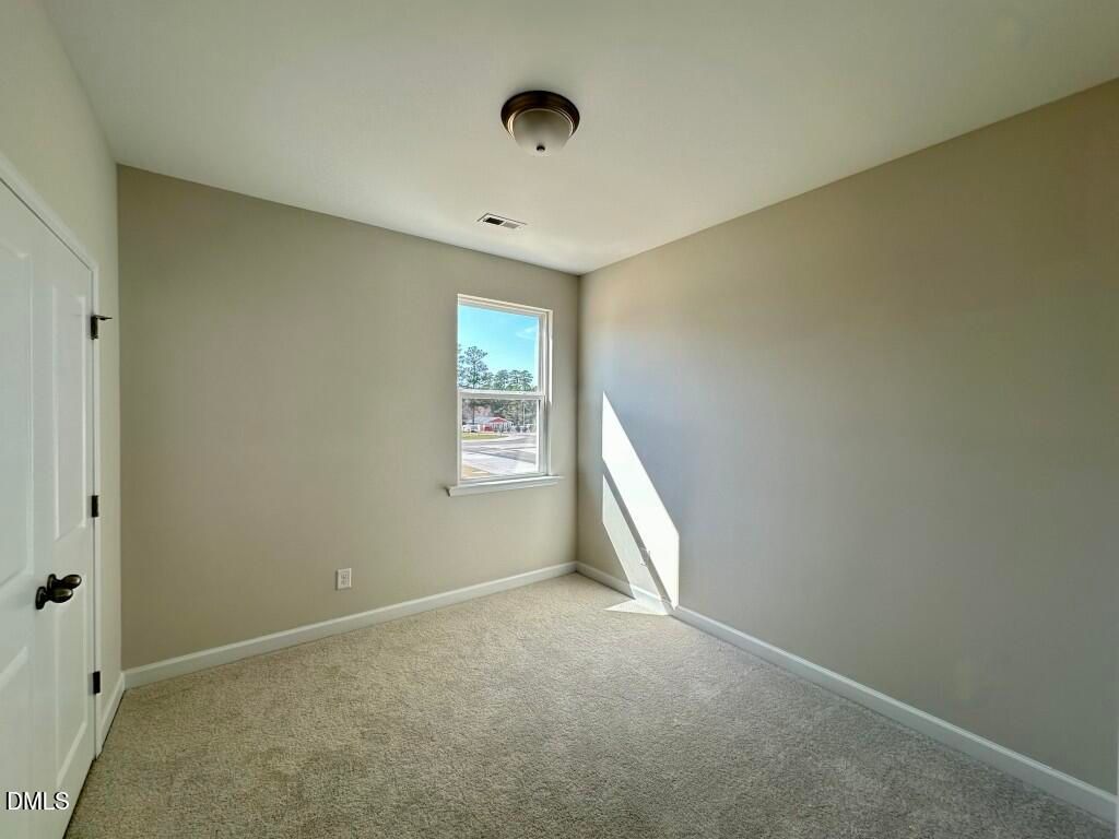 Bright secondary bedroom with beige walls, carpet flooring, and sunny window in Davidson Homes The Burke, Knightdale, NC