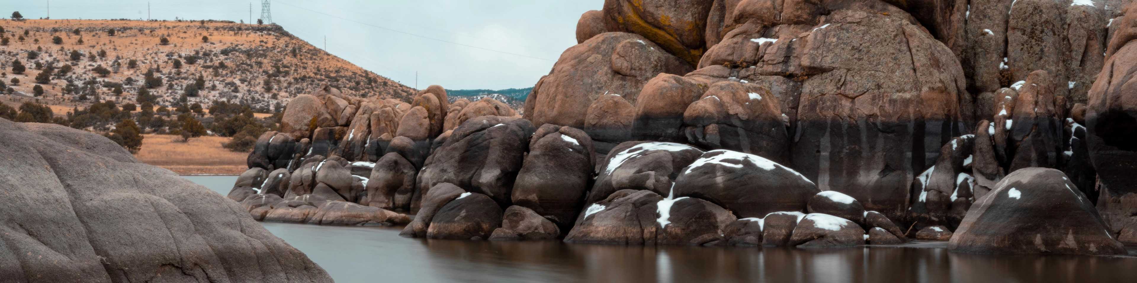 Snow-dusted granite boulders and serene lake under cloudy skies in Prescott Region