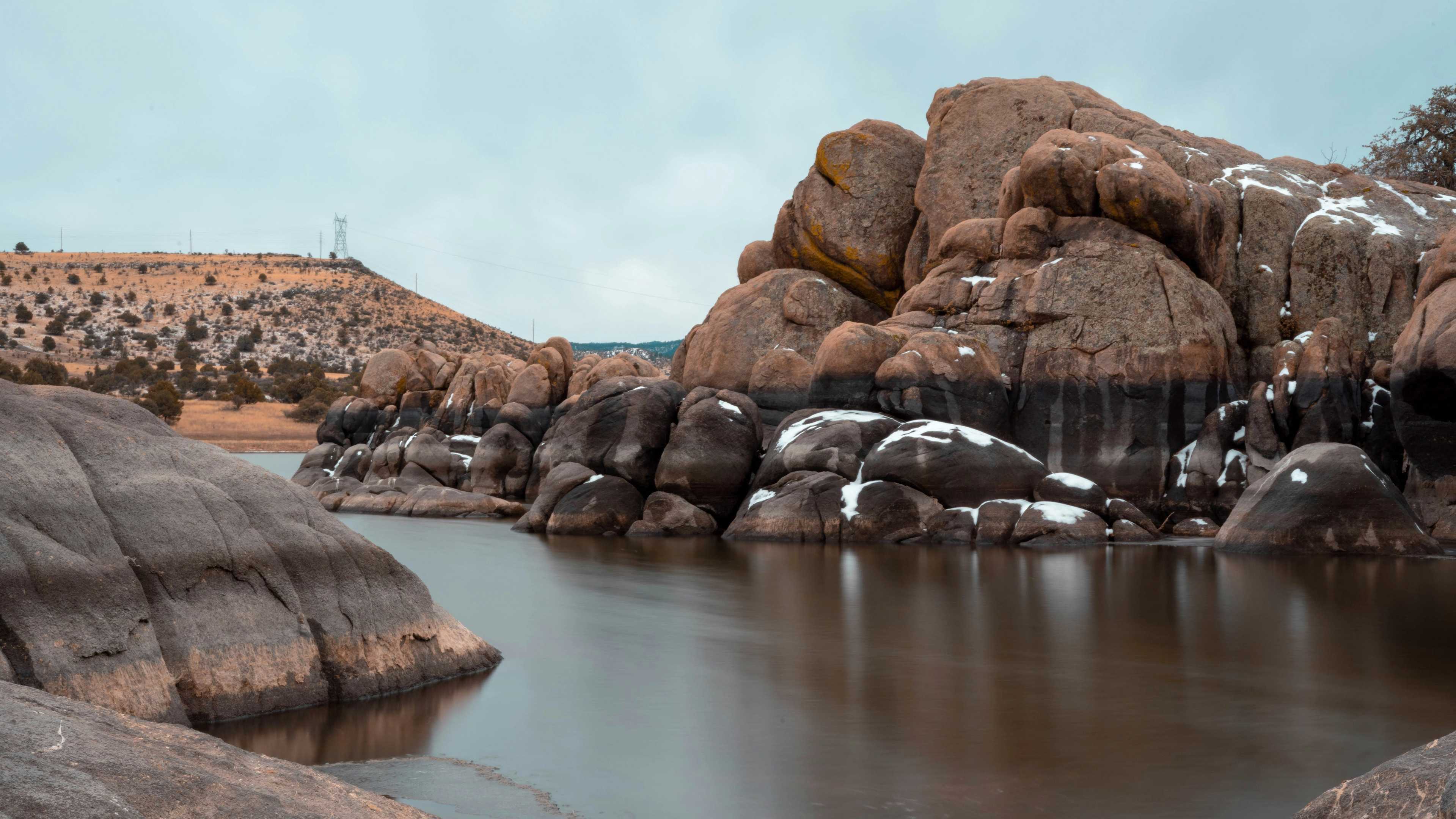 Snow-dusted granite boulders and serene lake under cloudy skies in Prescott Region
