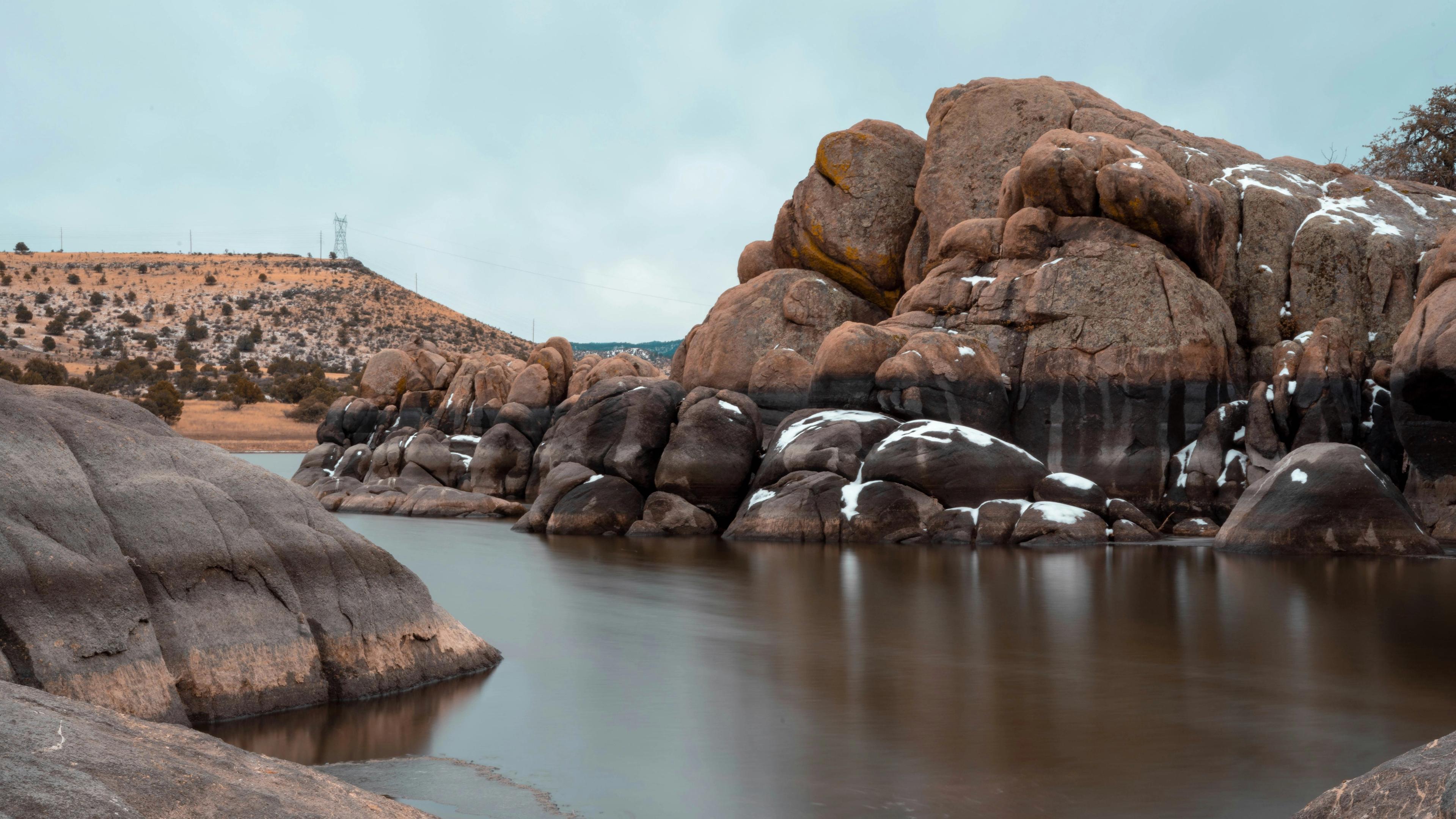 Snow-dusted granite boulders and serene lake under cloudy skies in Prescott Region