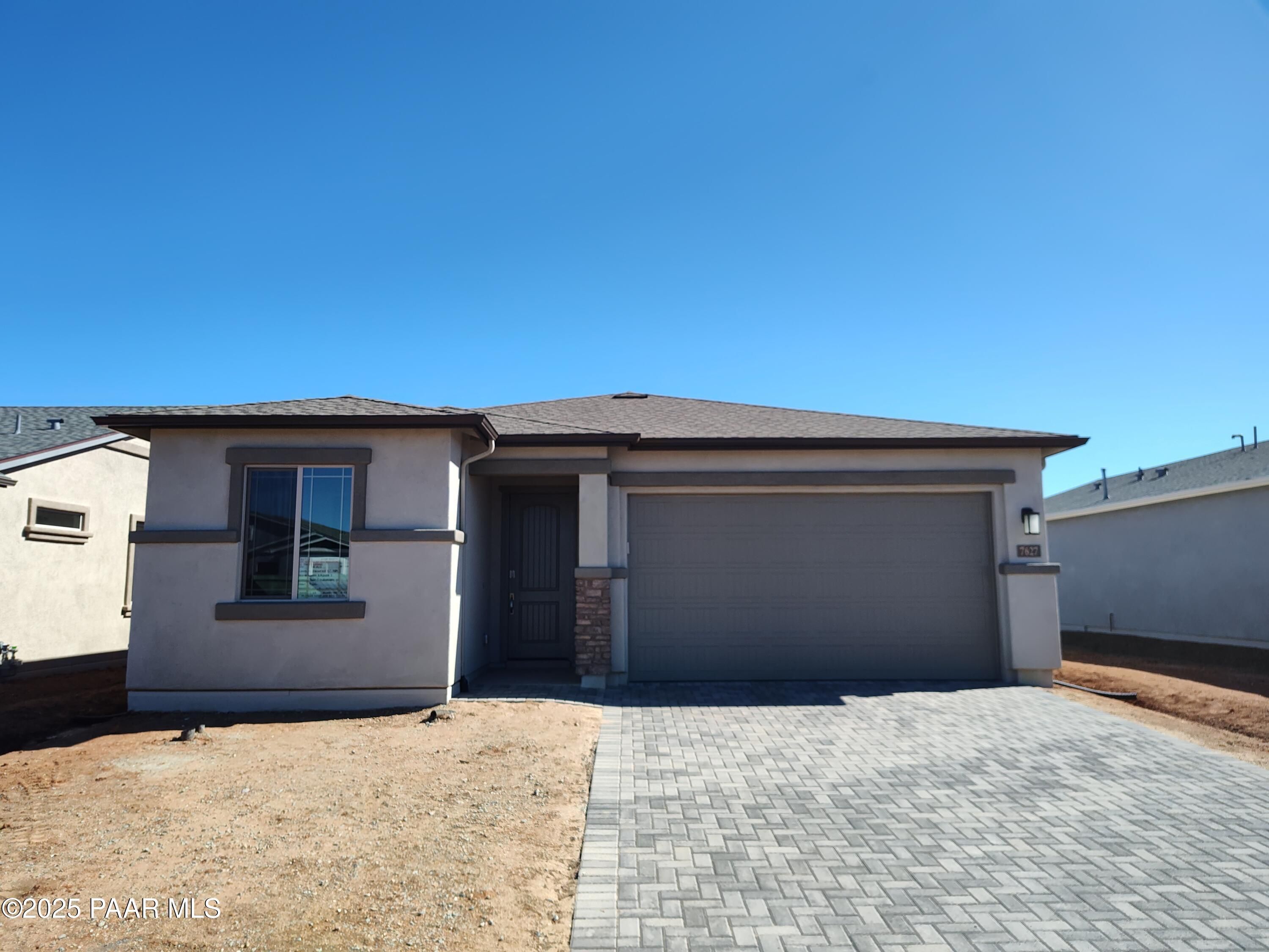 Modern 1-story home with 3-car garage, beige stucco exterior and paver driveway in North Ridge at Pronghorn Ranch, Prescott Valley, Arizona