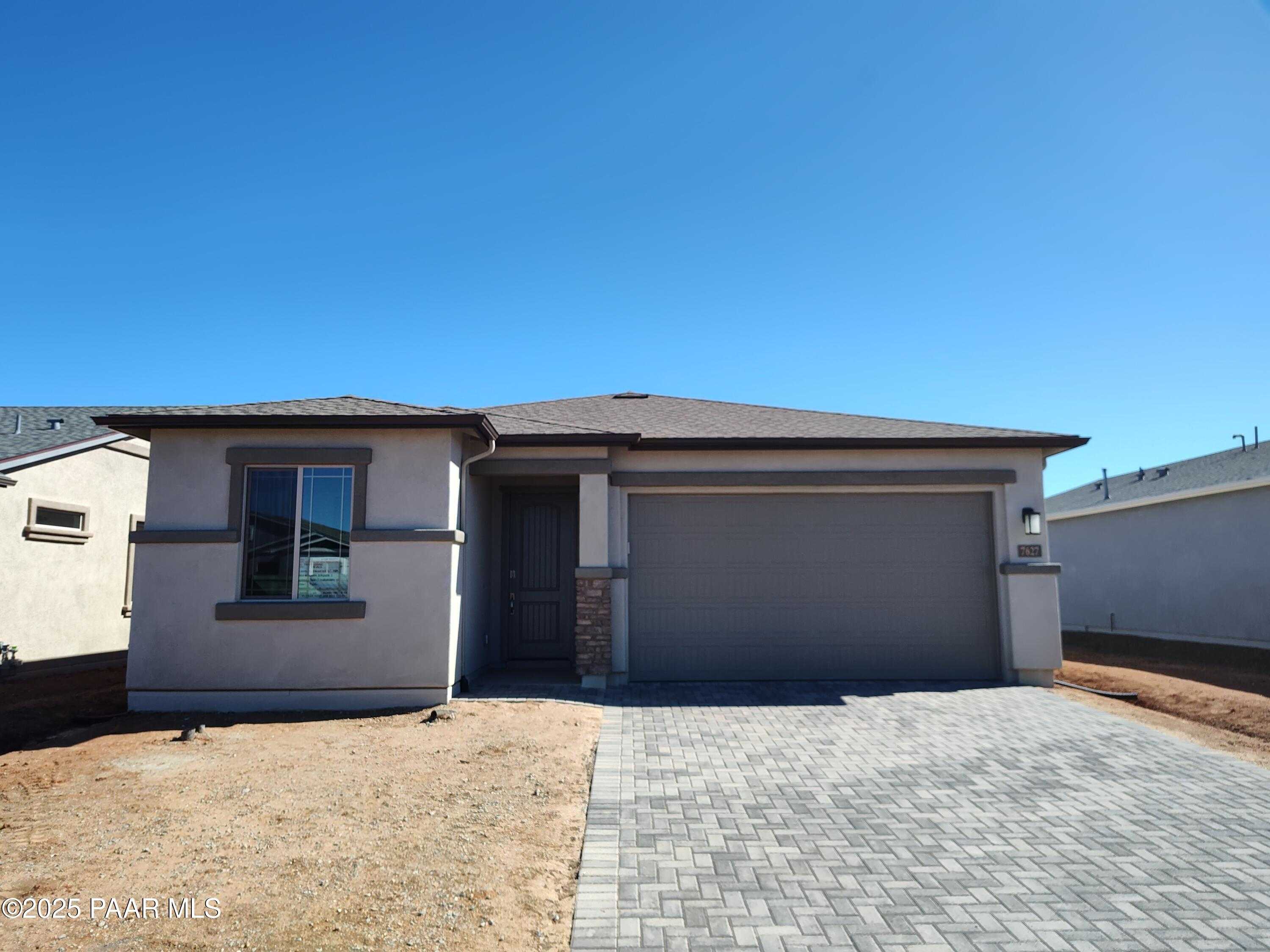 Modern 1-story home with 3-car garage, beige stucco exterior and paver driveway in North Ridge at Pronghorn Ranch, Prescott Valley, Arizona
