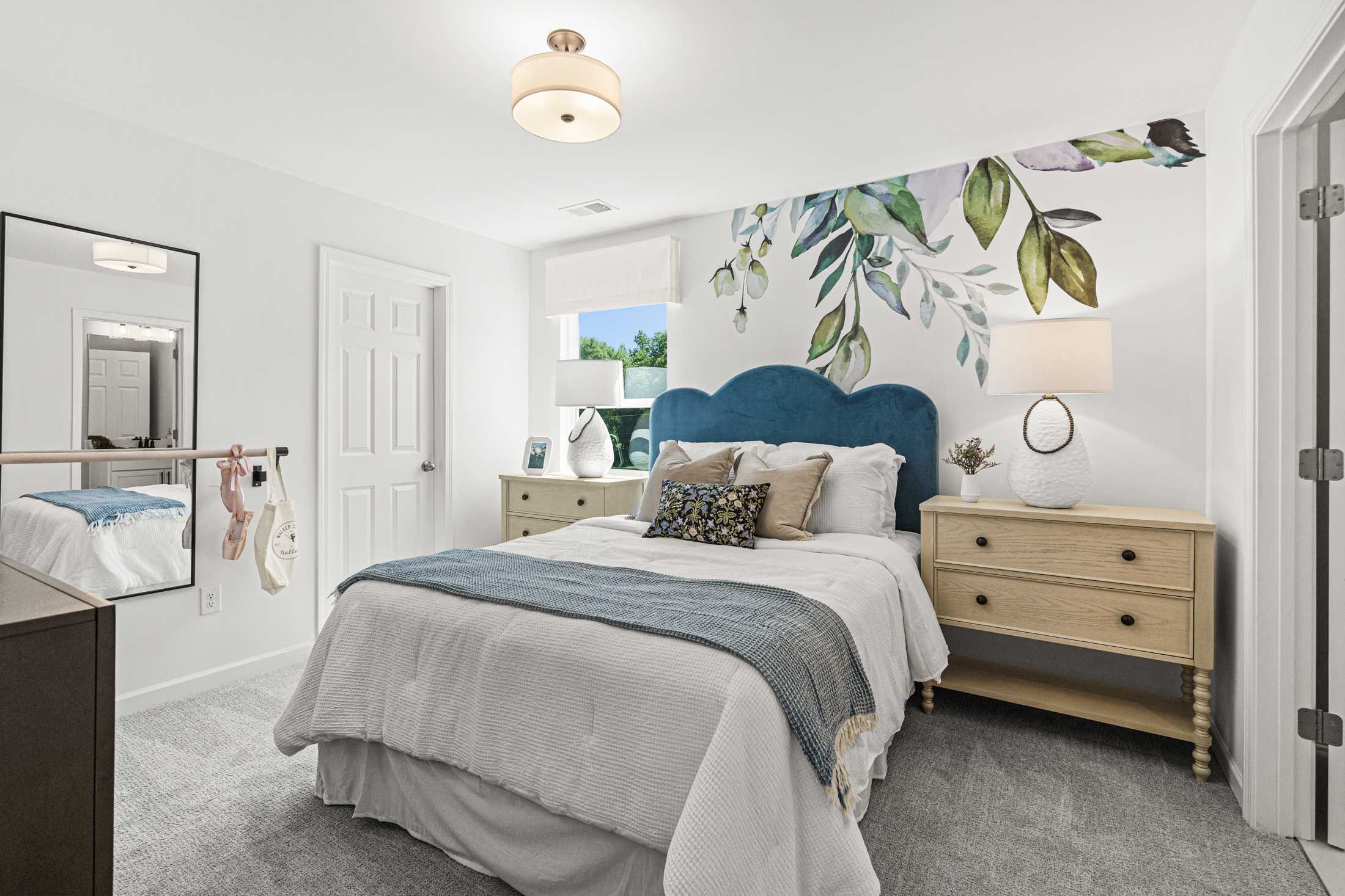 Spacious master bedroom in The Hickory A with blue velvet headboard bed, botanical leaf wall mural, and wooden nightstands