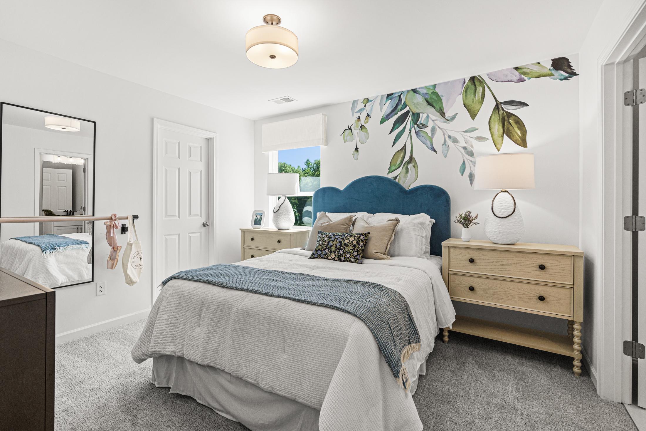 Spacious master bedroom in The Hickory B with blue velvet headboard, green leafy wallpaper, oak nightstands, and full-length mirror