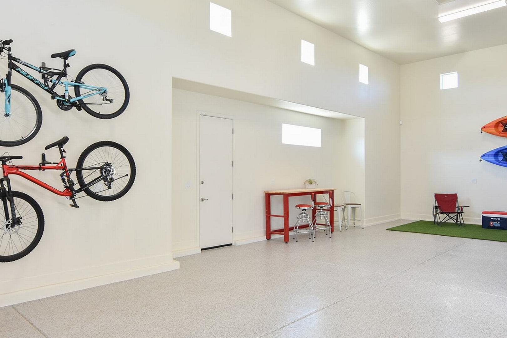 Spacious 3-car garage in The Summit E home by Evermore Homes with wall-mounted mountain bikes, kayaks, red table, stools, and turf rug