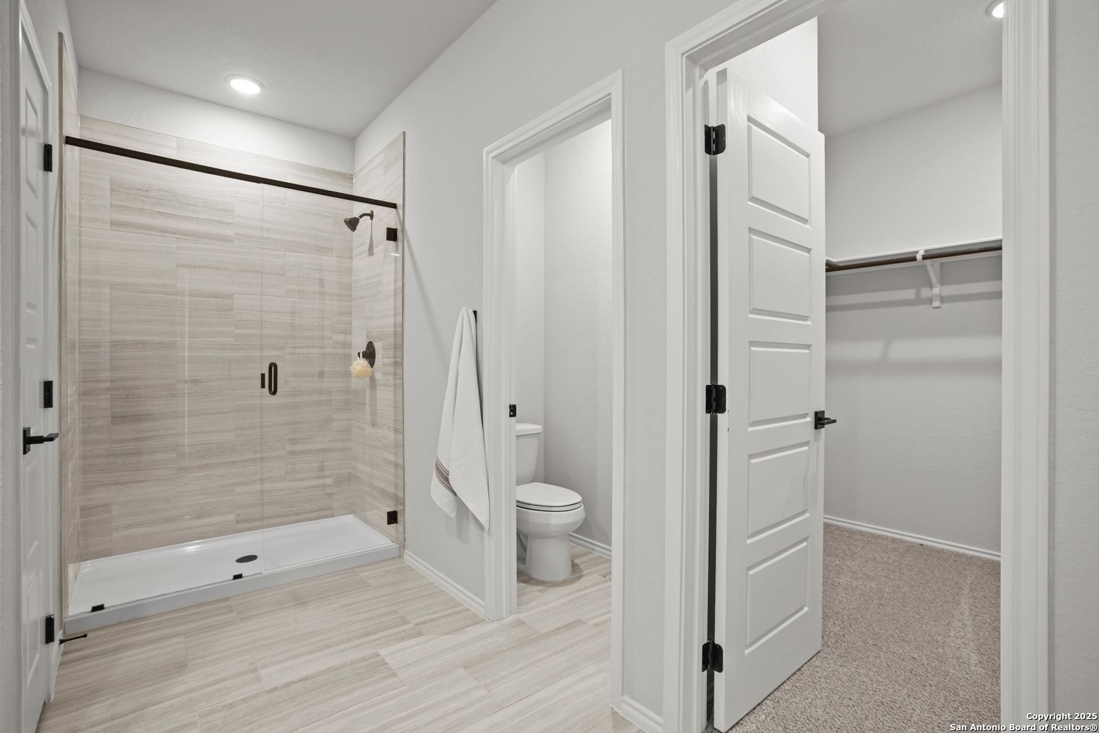 Modern master bathroom with frameless glass shower, tiled walls, and adjacent walk-in closet in Davidson Homes The Douglas C, Seguin, Texas
