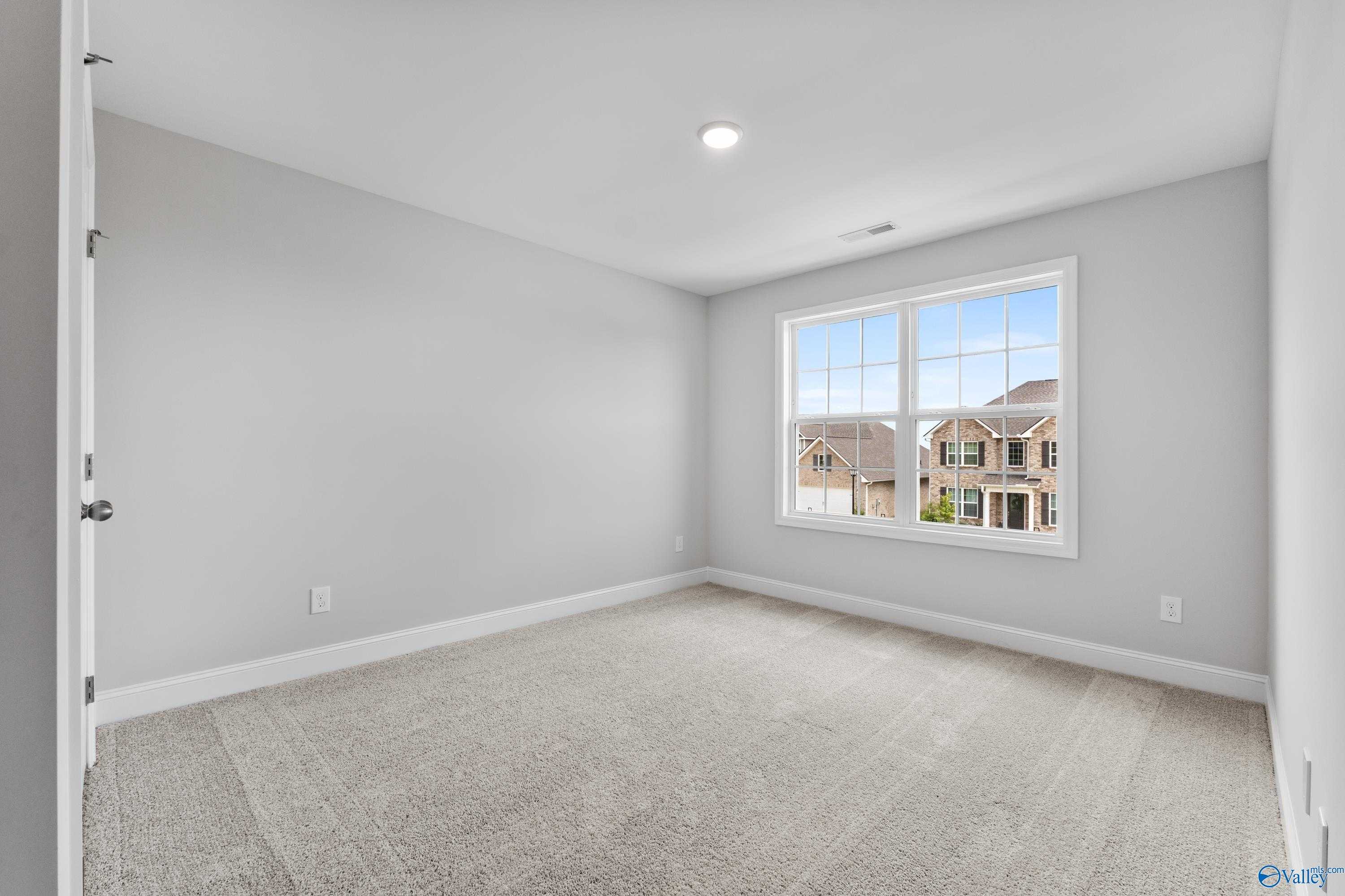 Bright empty secondary bedroom with light gray walls, neutral carpet, and window overlooking neighborhood in Davidson Homes Madison A, Toney, Alabama