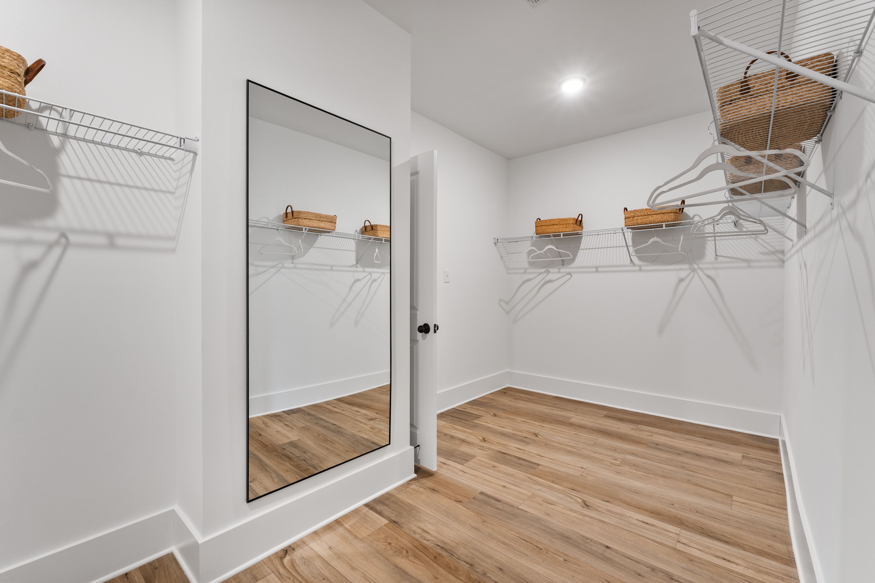 Spacious walk-in closet at River Road Estates in Decatur, Alabama with white walls, hardwood floors, full-length mirror, and wicker basket shelving
