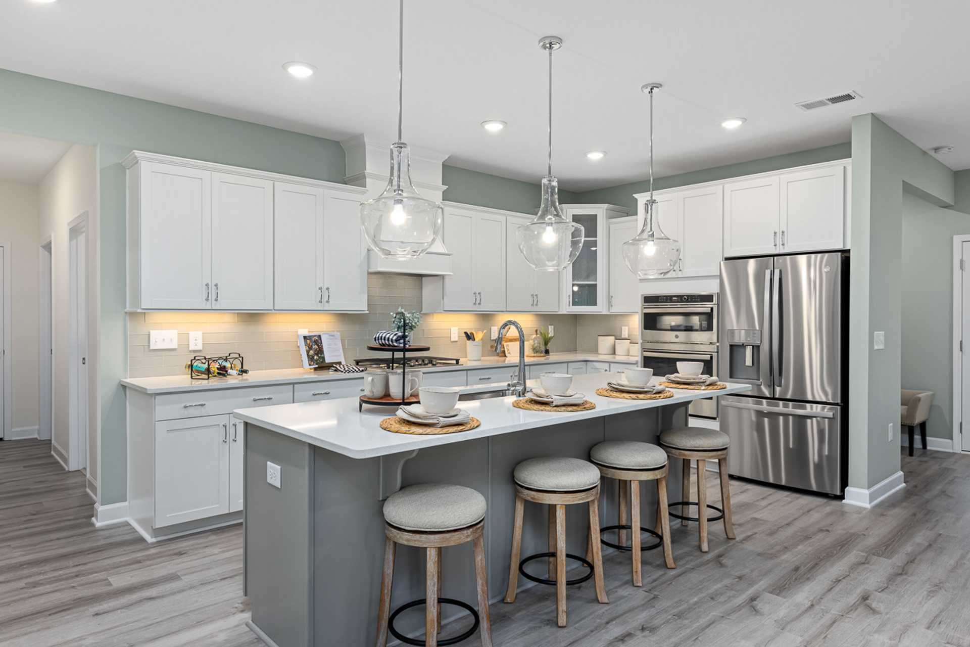Modern kitchen in Bentwinds Fuquay-Varina NC with white cabinets, gray island, pendant lights, stainless appliances, hardwood floors