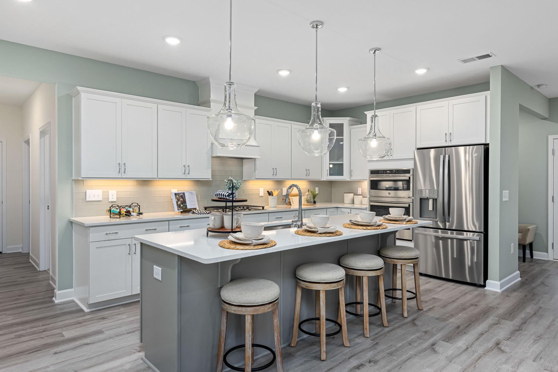 Modern kitchen in Bentwinds Fuquay-Varina NC with white cabinets, gray island, pendant lights, stainless appliances, hardwood floors