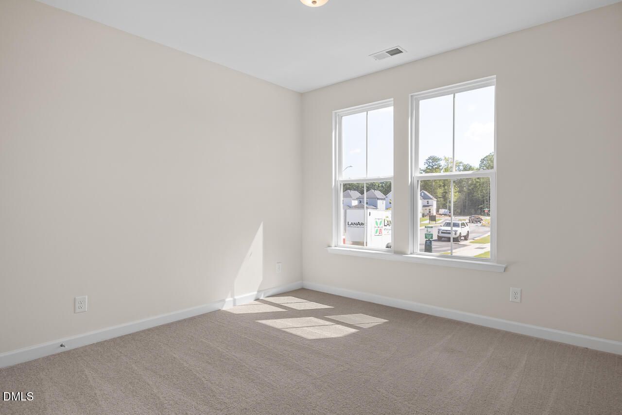 Bright empty bedroom with beige carpet and dual windows overlooking the neighborhood in Davidson Homes' The Mitchell plan, Knightdale, NC