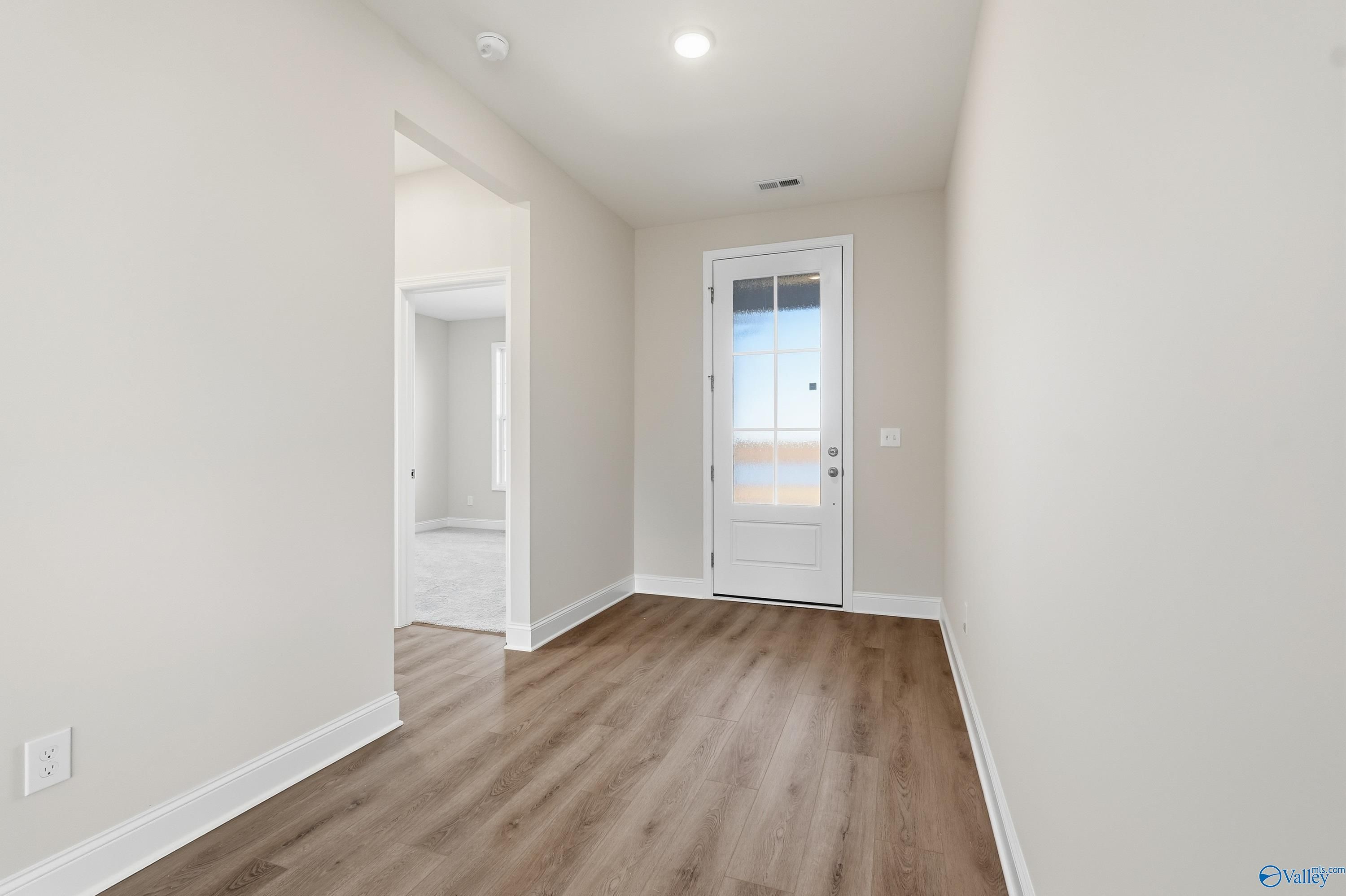 Bright entry hallway with neutral beige walls, luxury vinyl plank flooring, and white glass-paneled door in The Montgomery B, Toney, Alabama