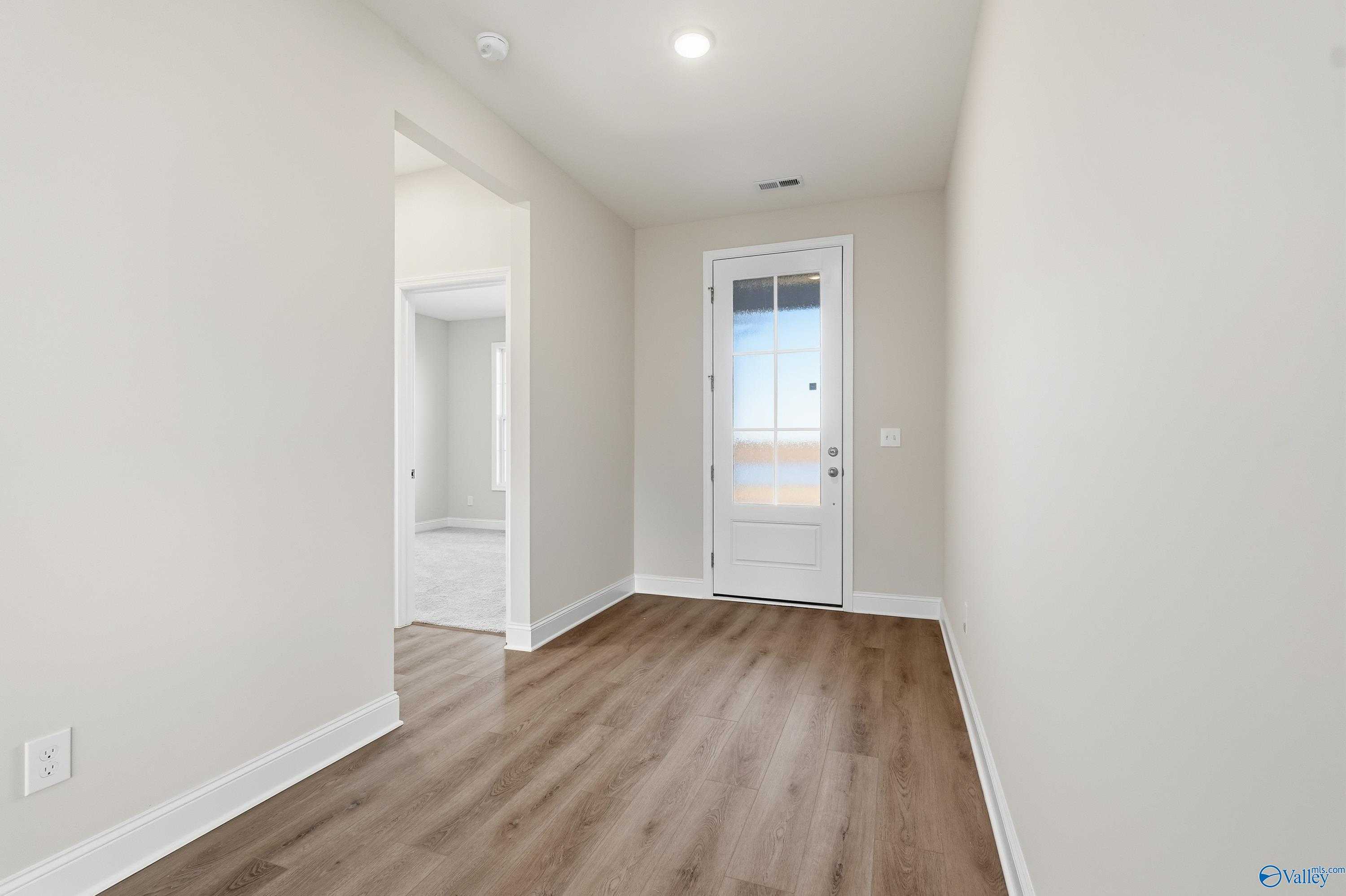 Bright entry hallway with neutral beige walls, luxury vinyl plank flooring, and white glass-paneled door in The Montgomery B, Toney, Alabama
