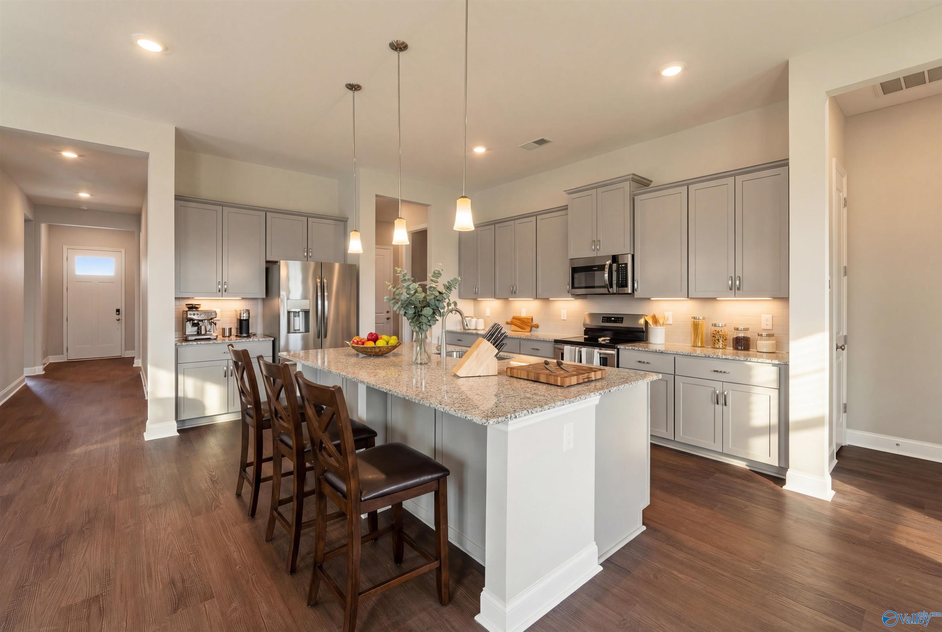 Open-concept kitchen with gray cabinets, granite island, stainless appliances, and bar stools in The Arcadia B, Riverton Preserve, Huntsville