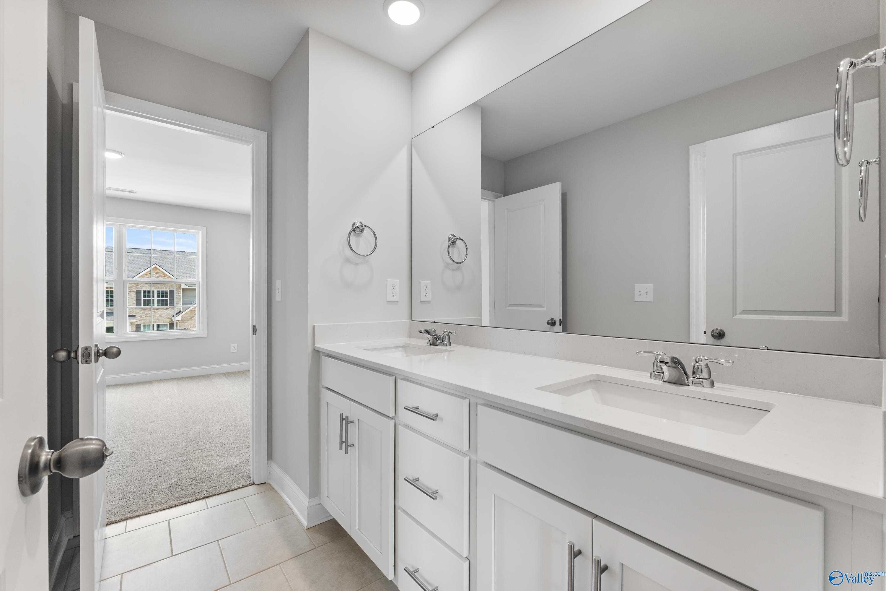 Modern master bathroom with double white vanity, quartz countertop, large mirror, and bedroom access in Davidson Homes The Madison A, Toney, Alabama