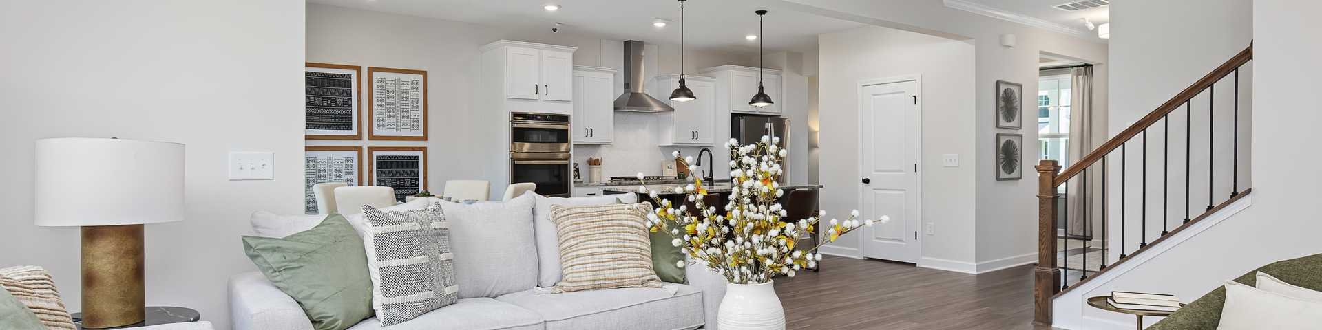 Spacious modern living room in new Four Oaks home with gray sofa, glass coffee table, vase, and open kitchen