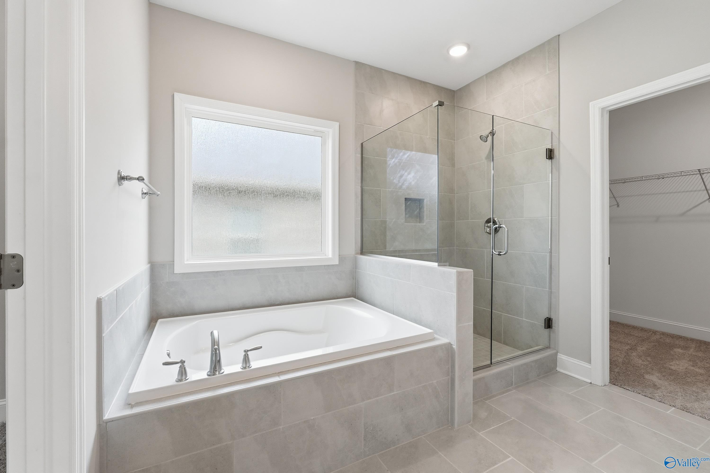 Elegant master bathroom featuring freestanding soaking tub, glass shower, and adjacent walk-in closet in Davidson Homes The Harrison B, Decatur, Alabama