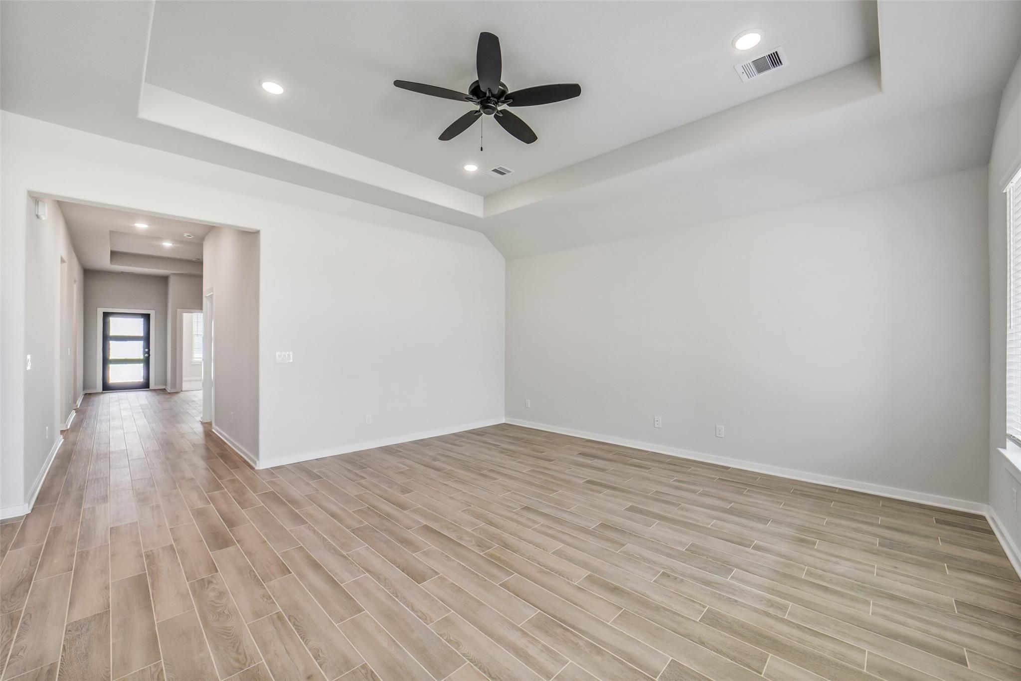 Spacious living room with tray ceiling, black ceiling fan, and light wood-look tile floors in Davidson Homes Acadia C, Magnolia TX